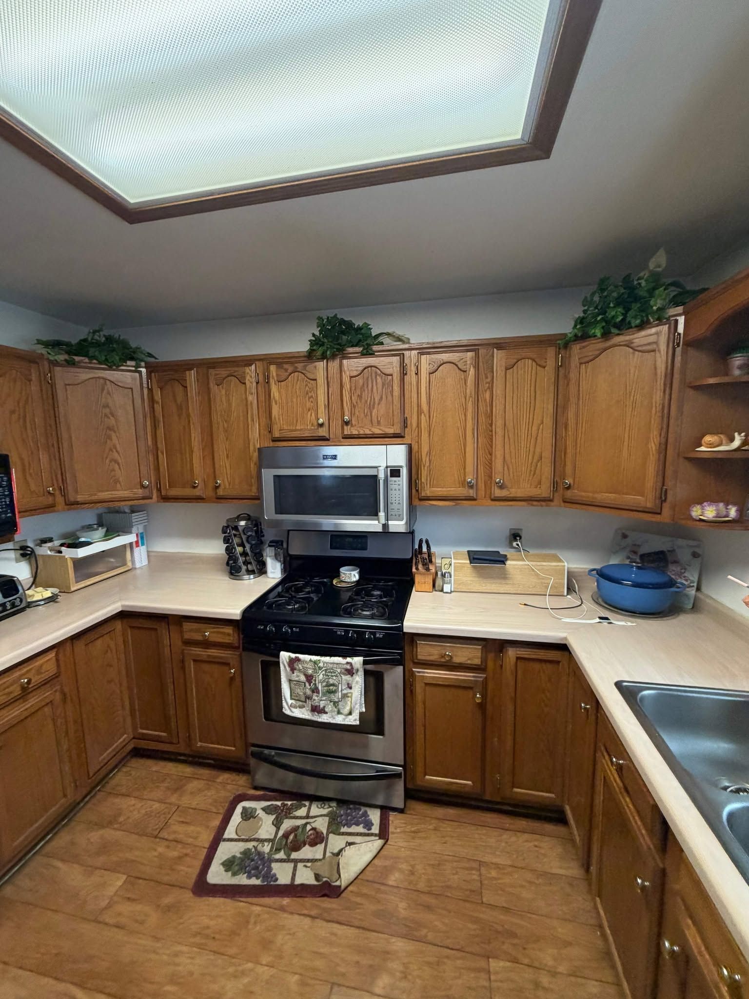 Small kitchen with wooden cabinets, stainless steel stove and microwave, beige counters, and a skylight.