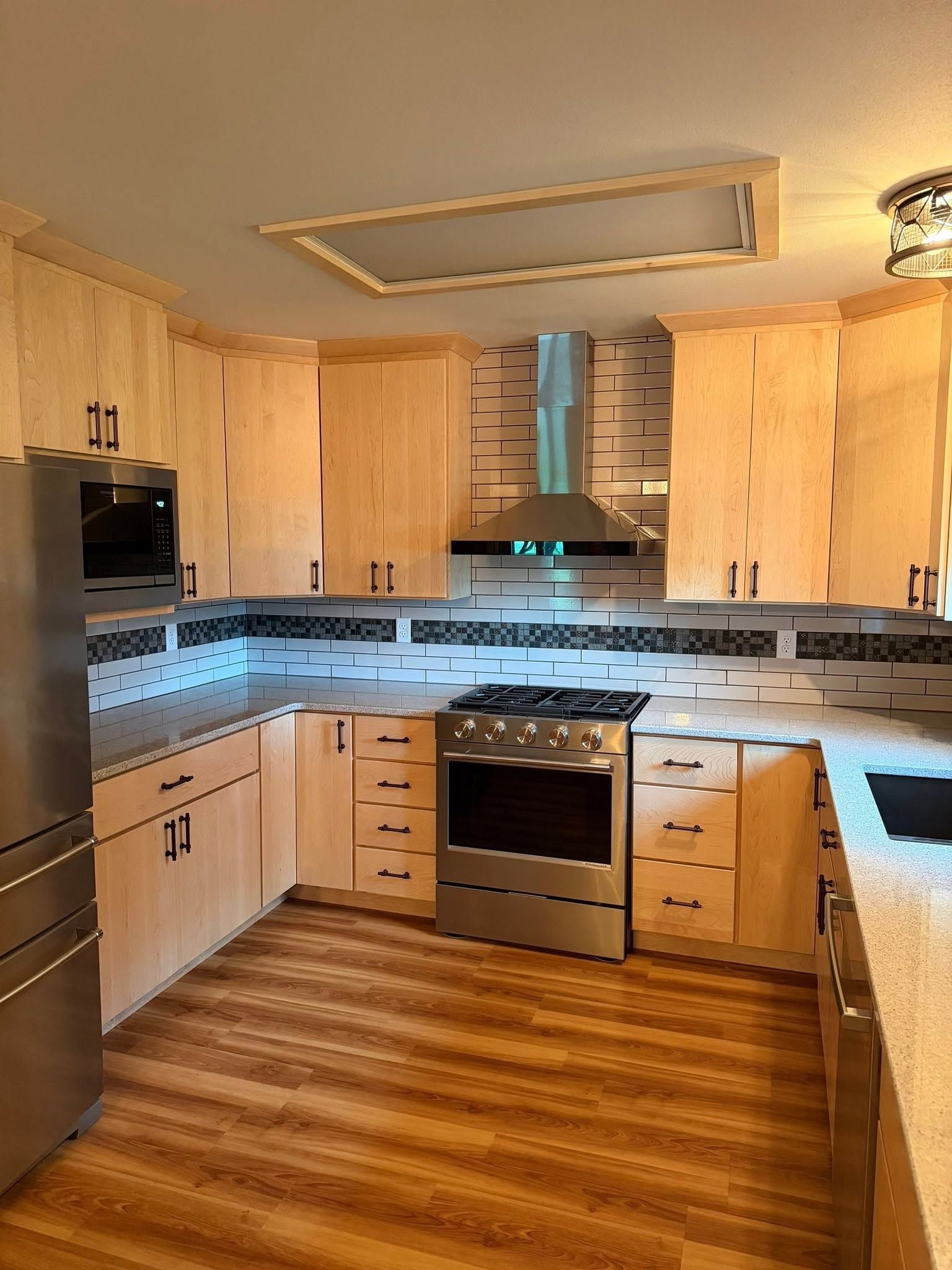 Modern kitchen with light wood cabinets, stainless appliances, and wood-look floor