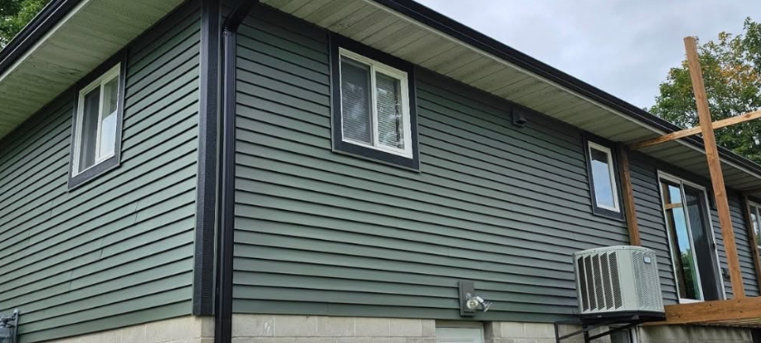Exterior of a house with green siding, white-trimmed windows, and a wooden deck with an air conditioner unit