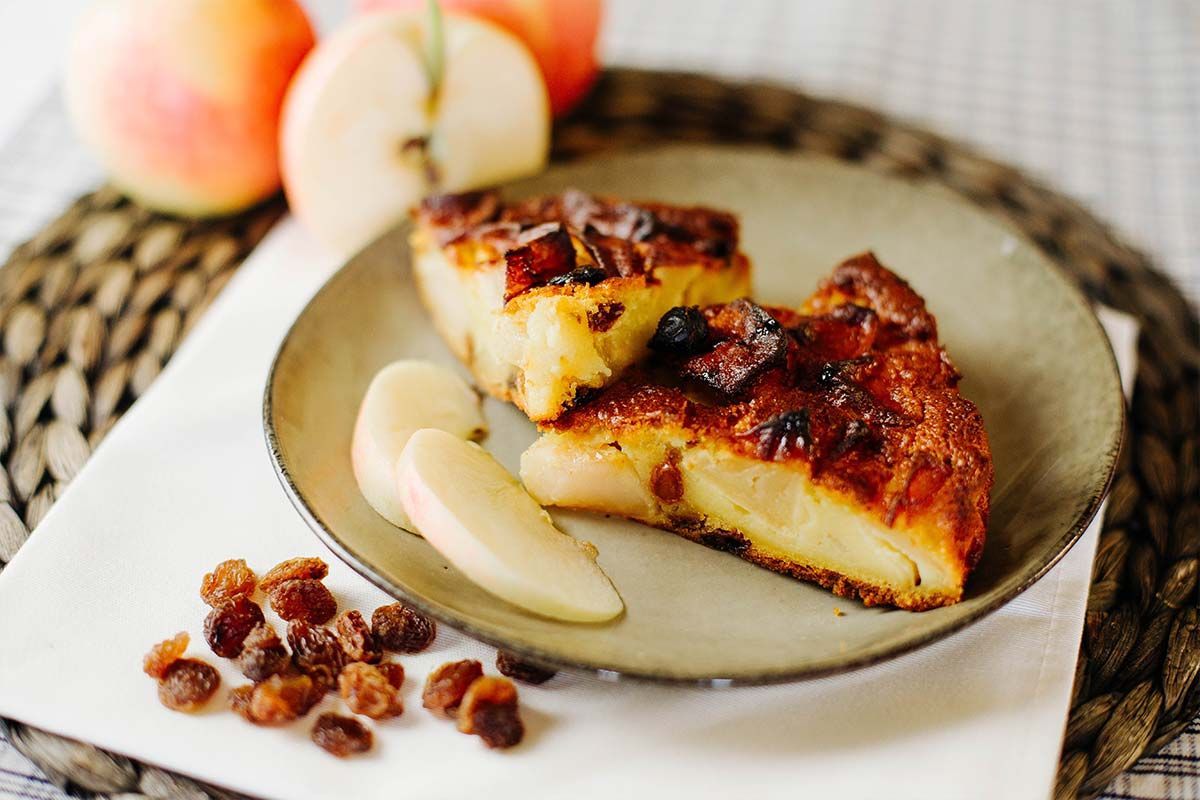 Una fetta di crostata di frutta caramellata su un piatto con fettine di pera e uvetta su una tovaglietta intrecciata.