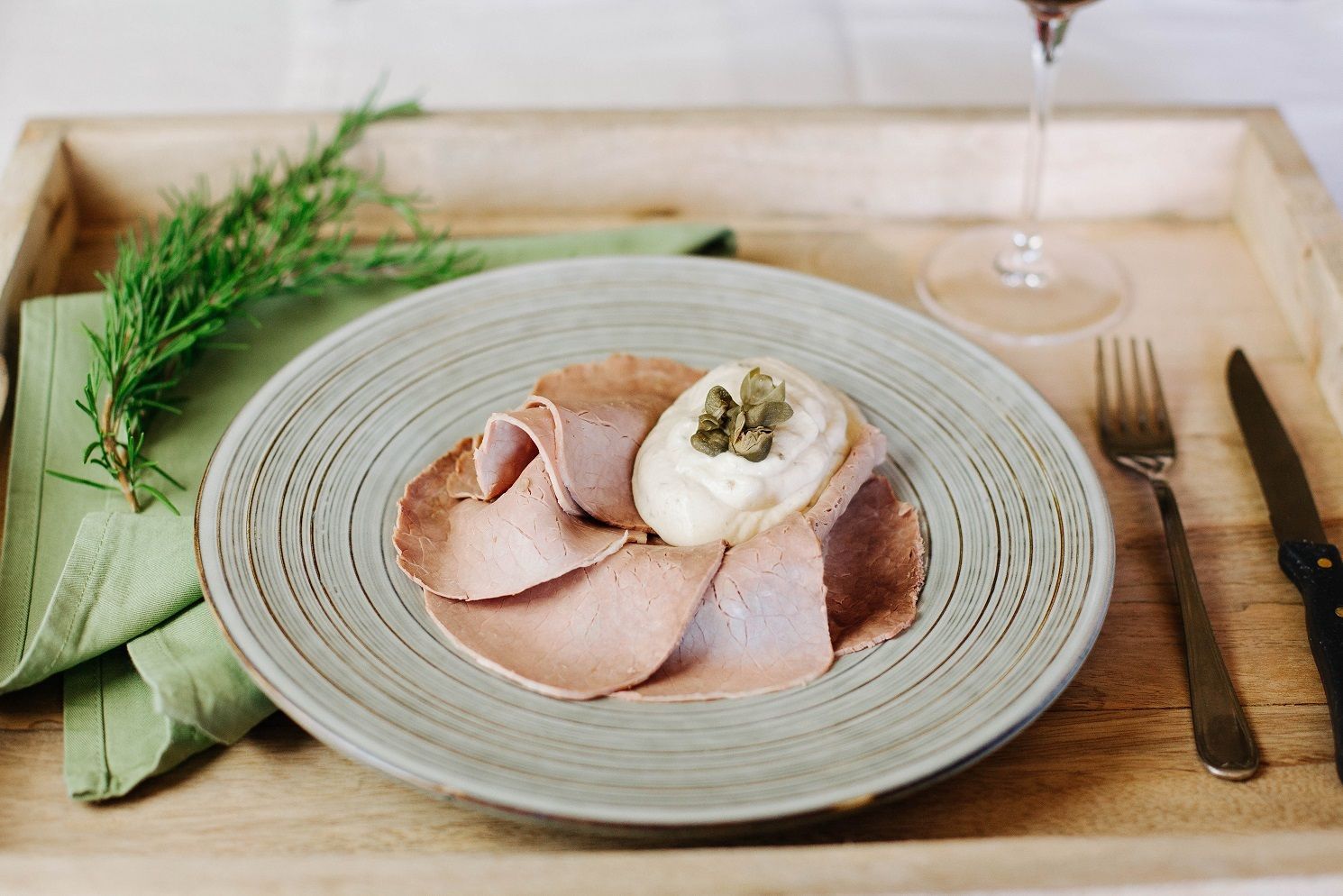 Affettati di salumi con uovo in camicia su un vassoio di legno rustico, con erbe aromatiche e posate a portata di mano.