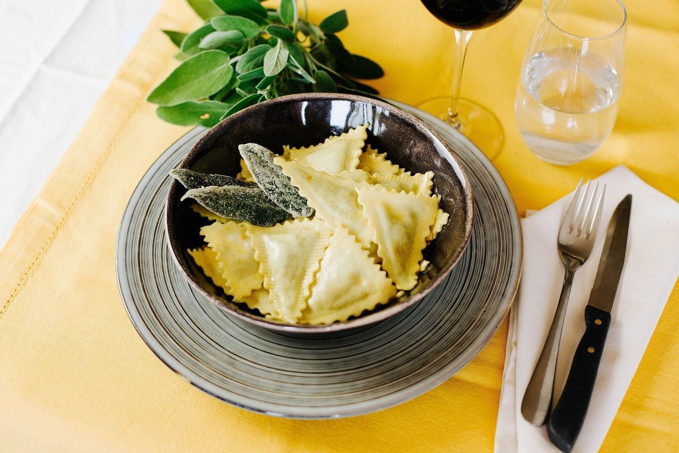 Pasta a farfalla in una ciotola su una tovaglia gialla con posate e un bicchiere nelle vicinanze.
