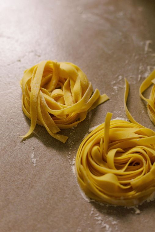 Due nidi di pasta gialla cruda su un piano di lavoro infarinato