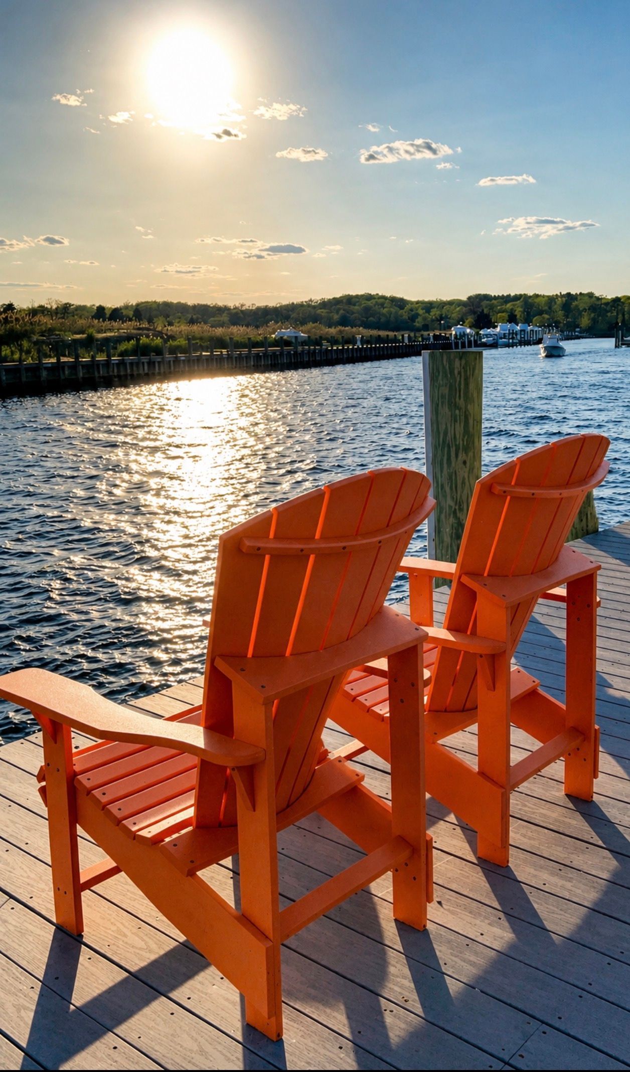 Two orange Adirondack chairs on a dock overlooking a sunlit lake at sunset
