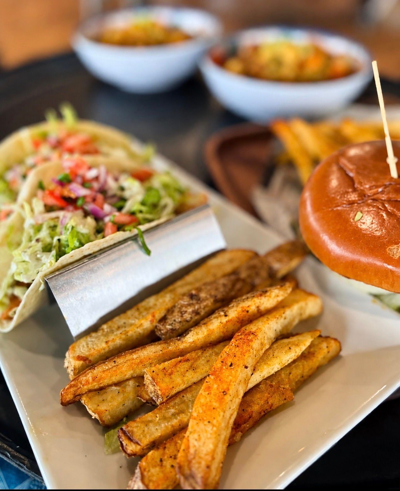 Plate with seasoned fries, salad, and a burger on a restaurant table with bowls in the background