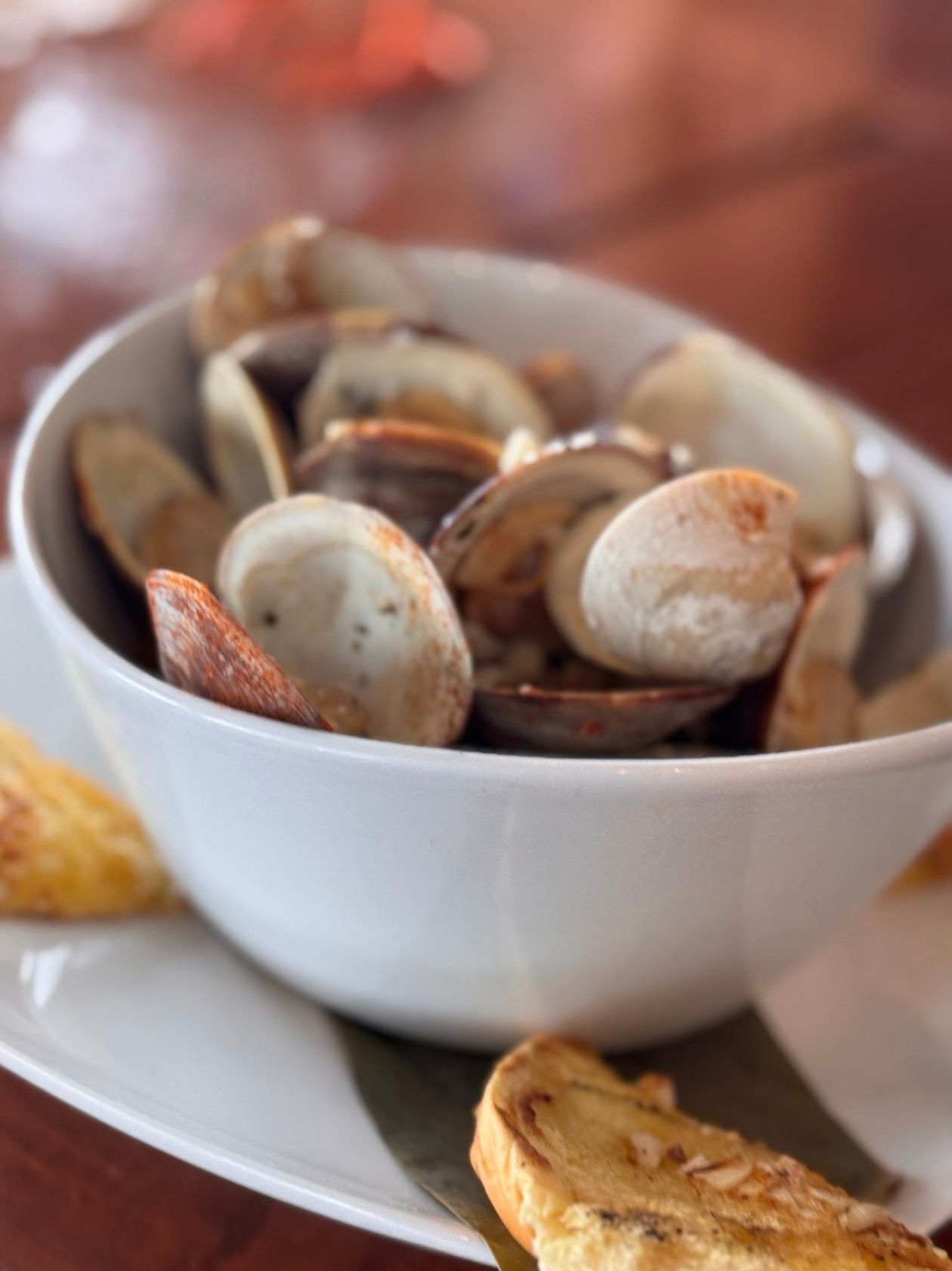 Bowl of steamed clams on a plate with bread slices beside it