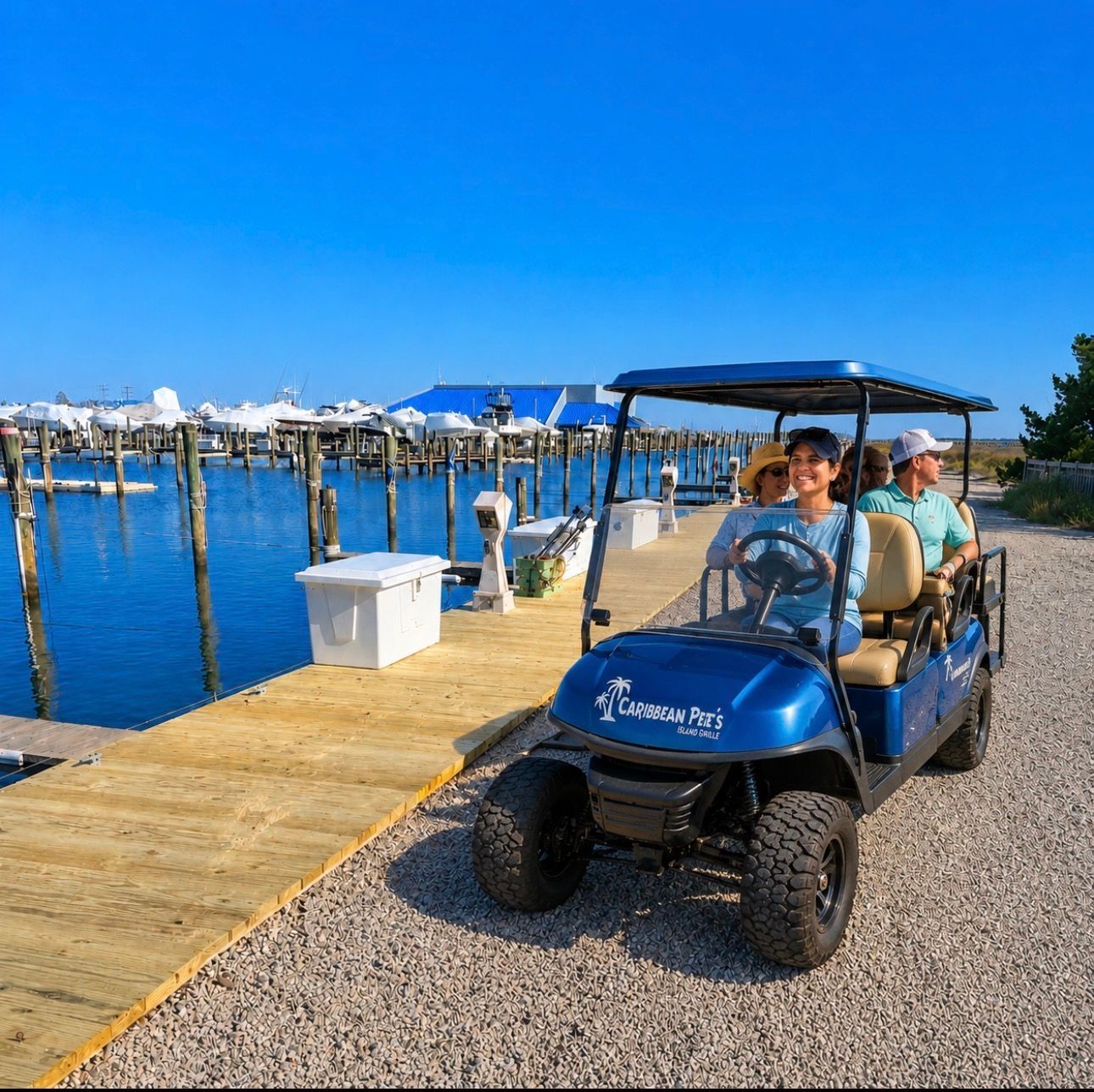 Blue golf cart with passengers on a dock by calm water under a clear sky