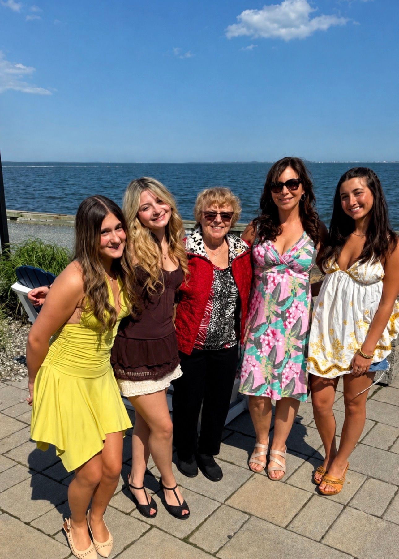 Five people smiling on a sunny waterfront promenade, with blue water and sky behind them.