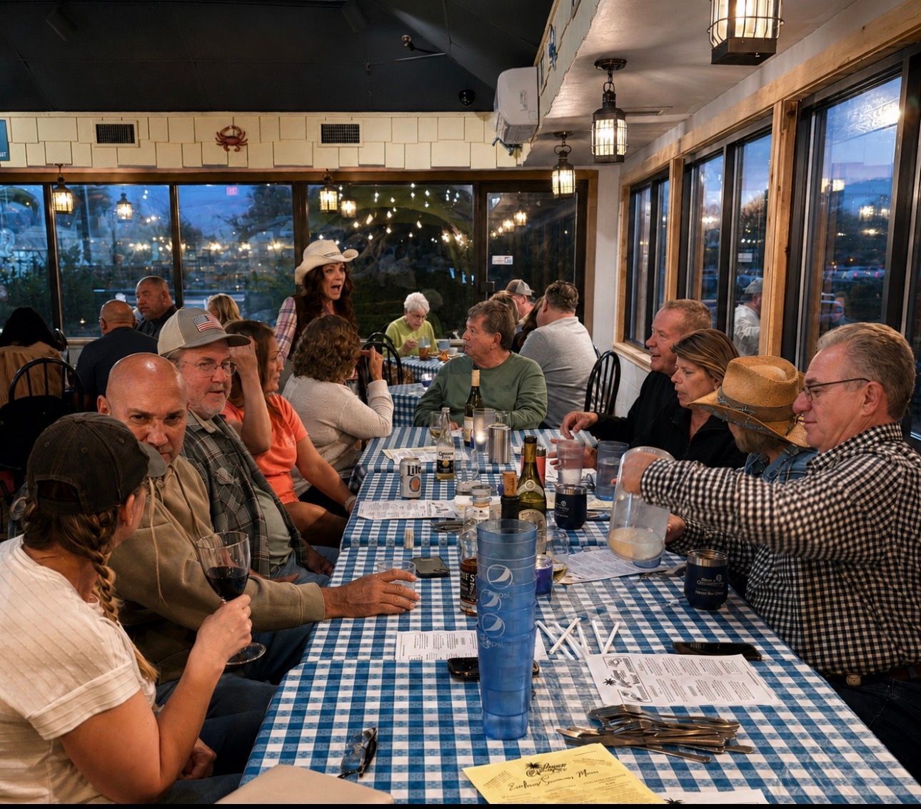 People seated at a long table in a warm-lit restaurant, eating, talking, and raising glasses together.
