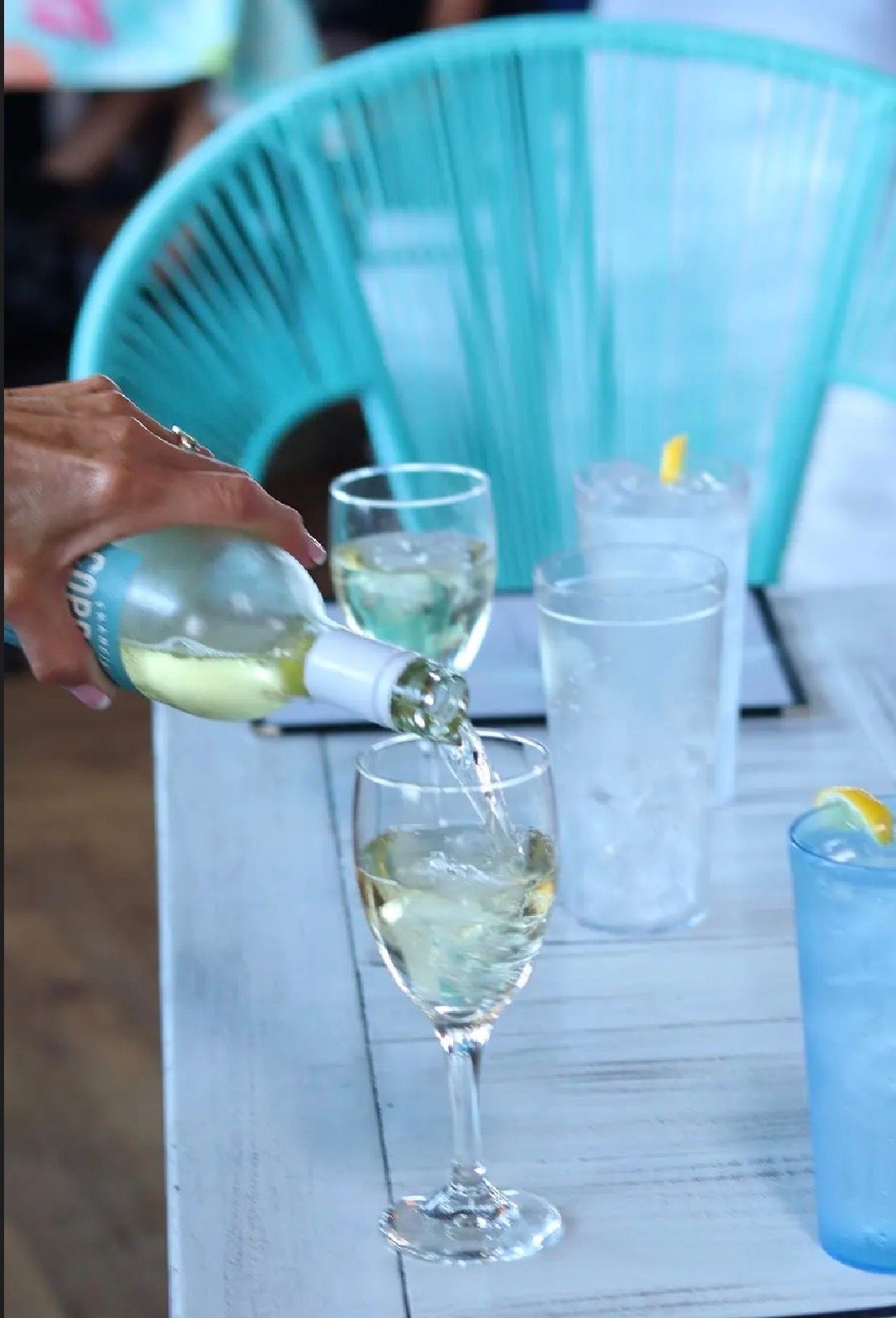 Pouring white wine into a stemmed glass at an outdoor table with colorful plastic chairs