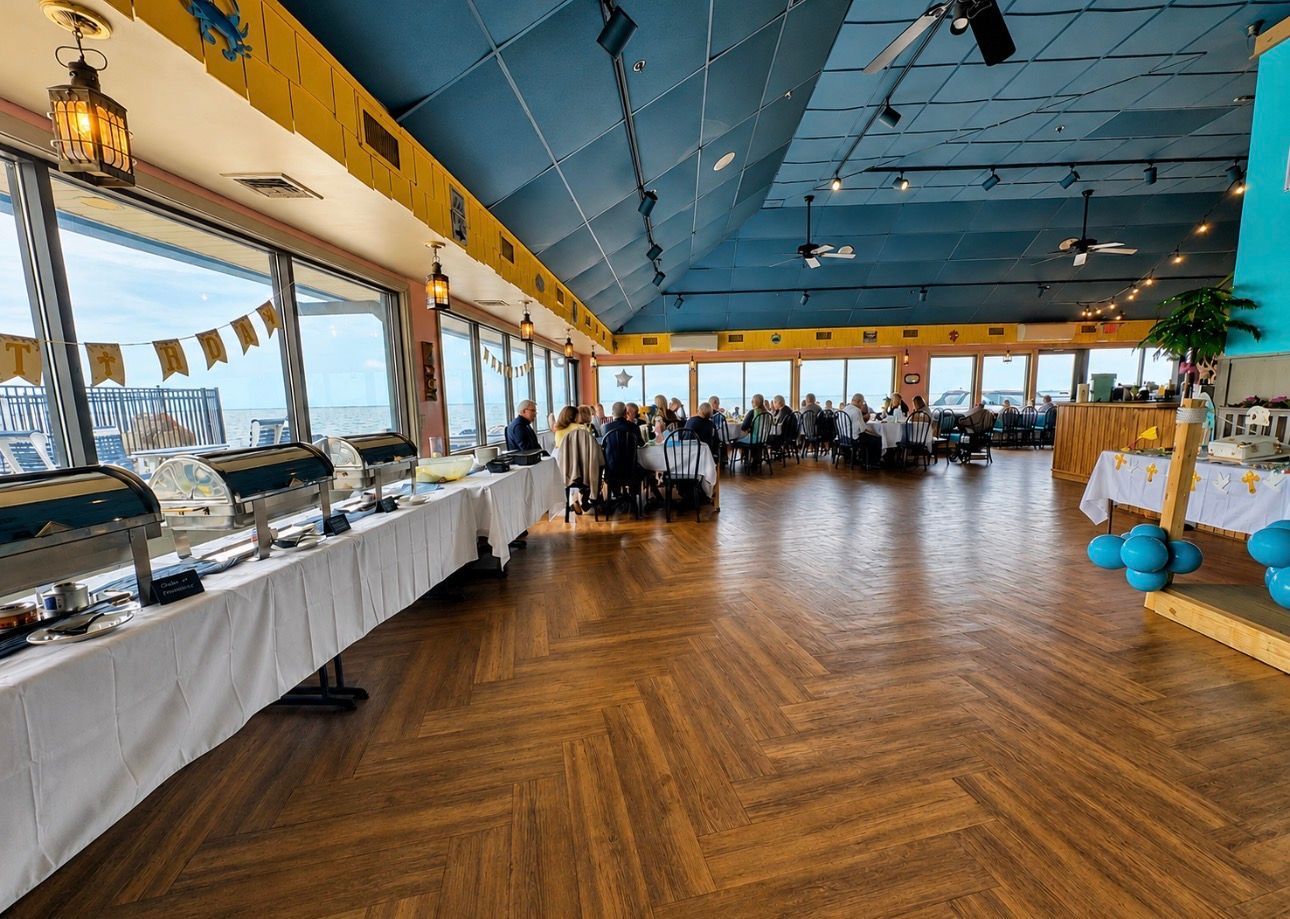Bright banquet hall with long buffet tables, blue ceiling, and guests seated at round tables by large windows