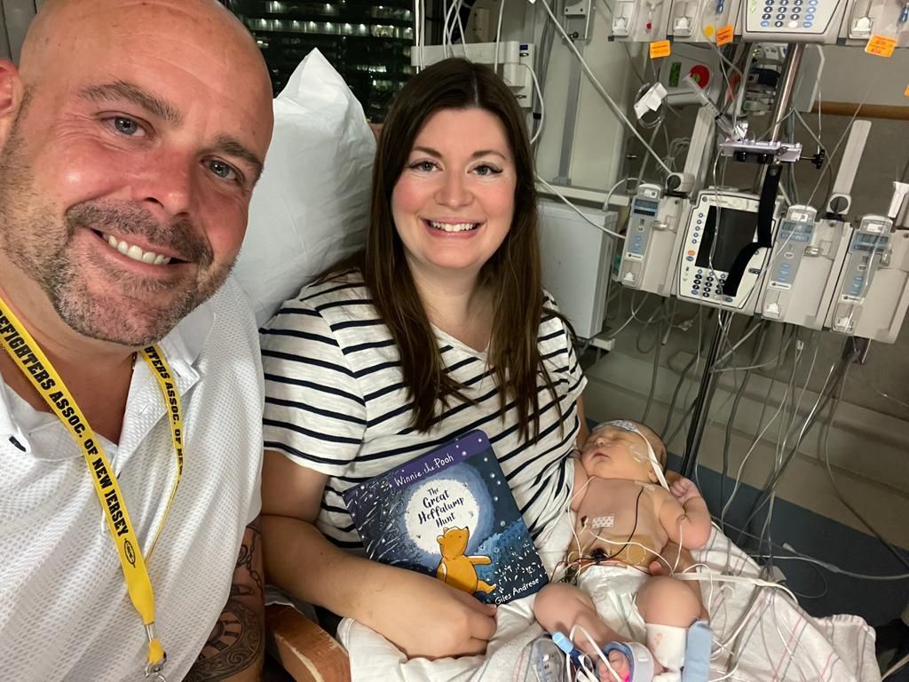 A man and a woman are sitting next to a baby in a hospital bed.