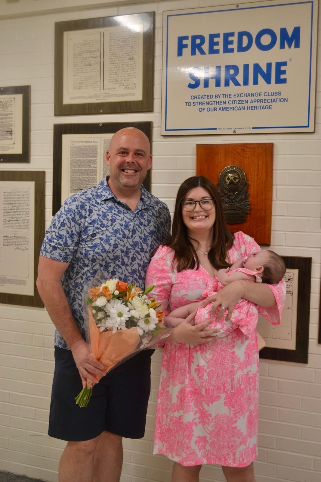 A man and a woman are holding a baby and a bouquet of flowers.