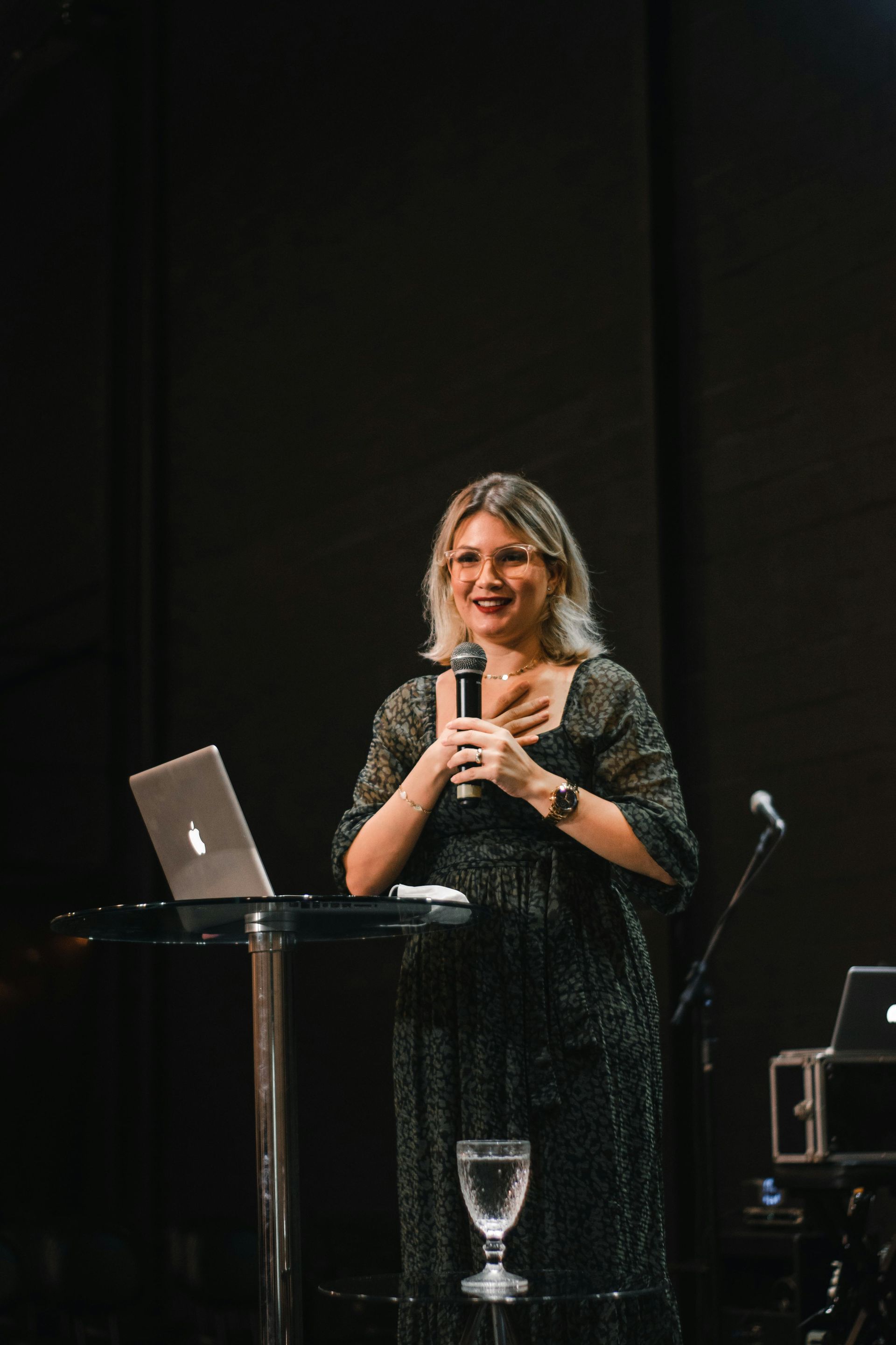 A woman is standing in front of a laptop and a microphone.