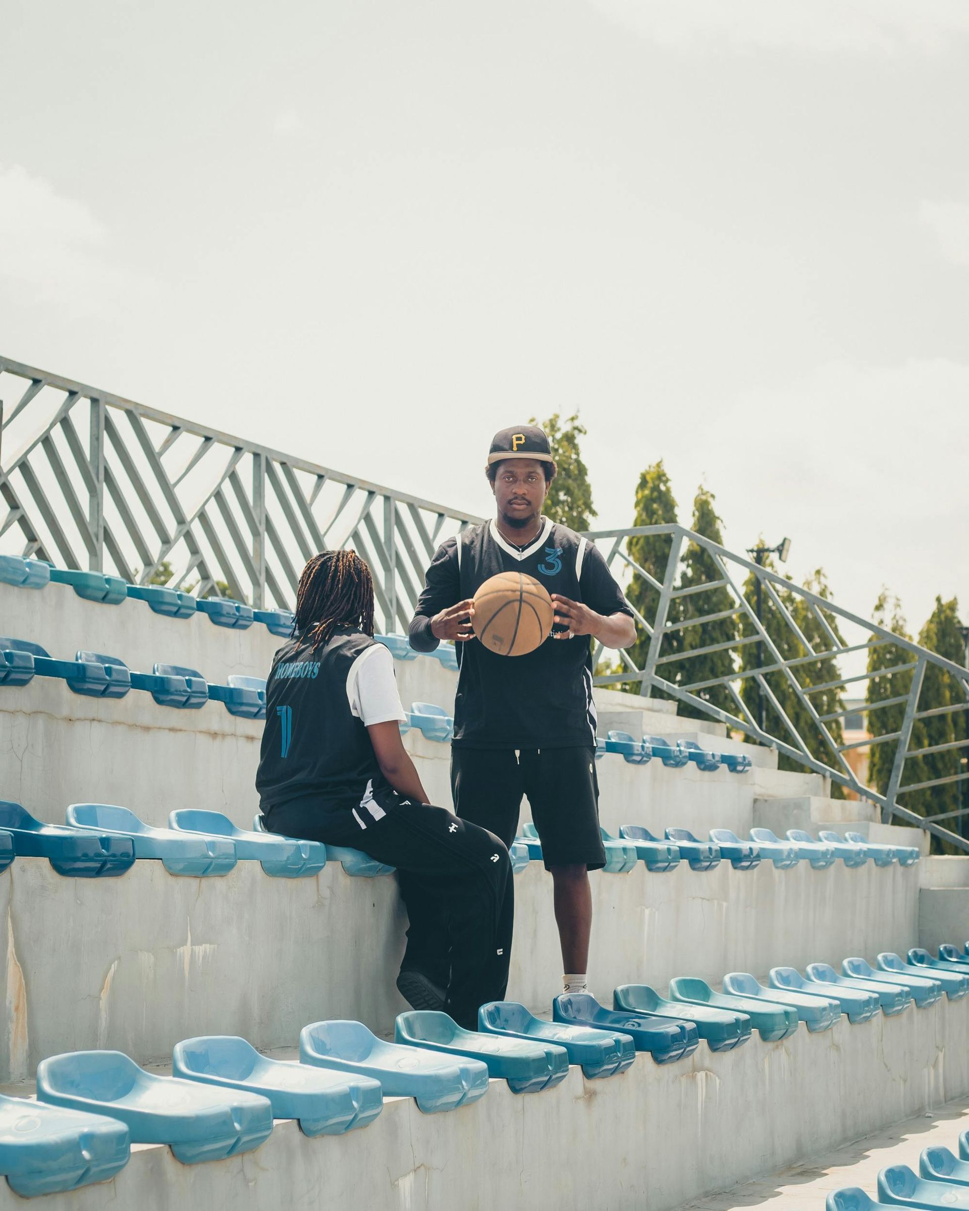 Two men are sitting on the bleachers of a stadium holding a basketball.