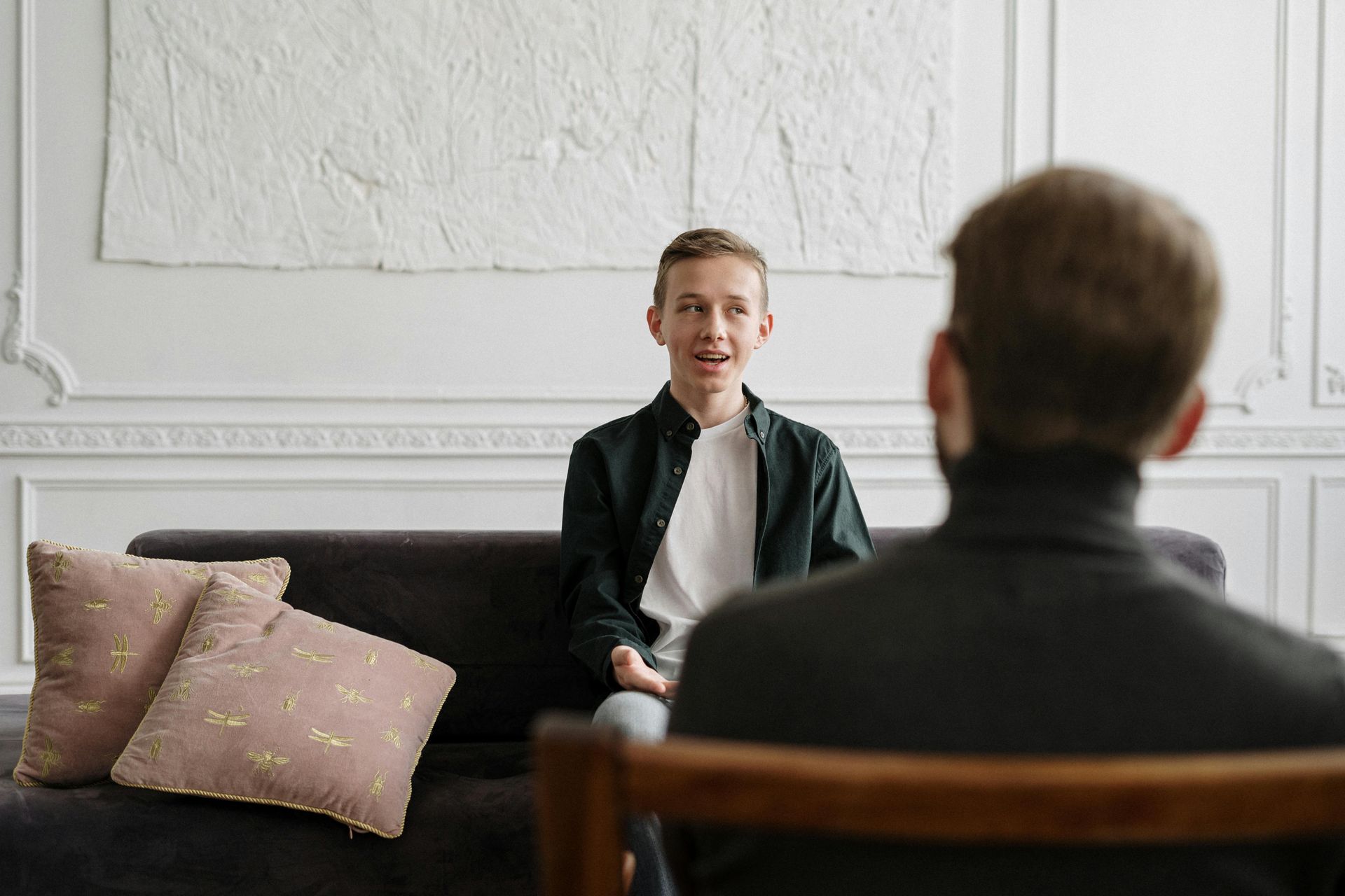 A man is sitting on a couch talking to a young boy.