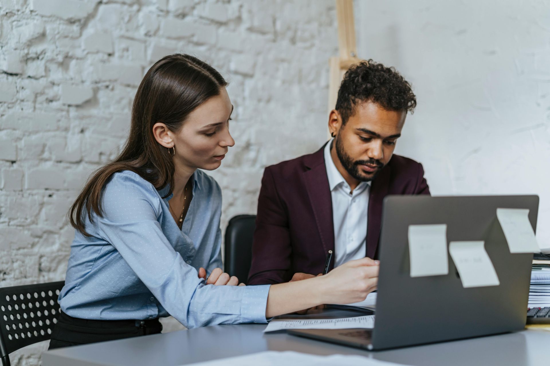 A man and a woman are sitting at a table looking at a laptop computer.