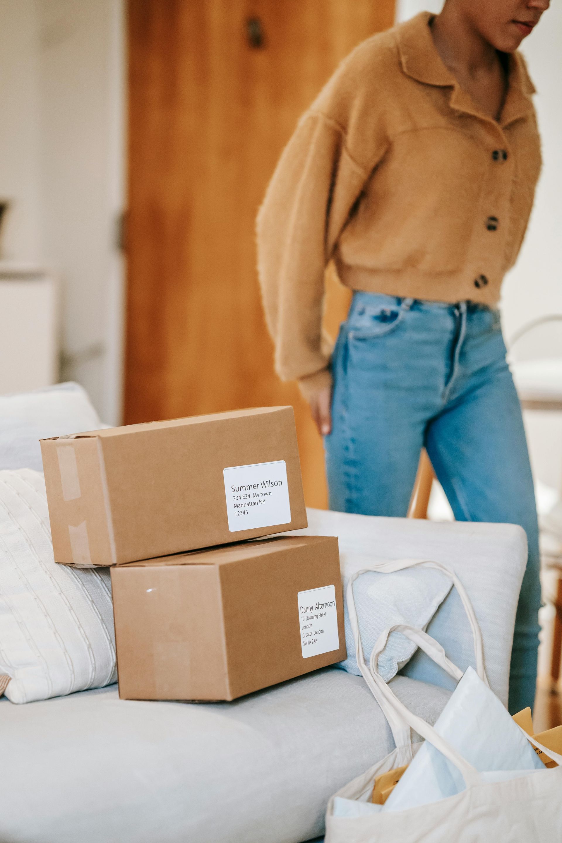 A woman is standing next to a couch with boxes on it.