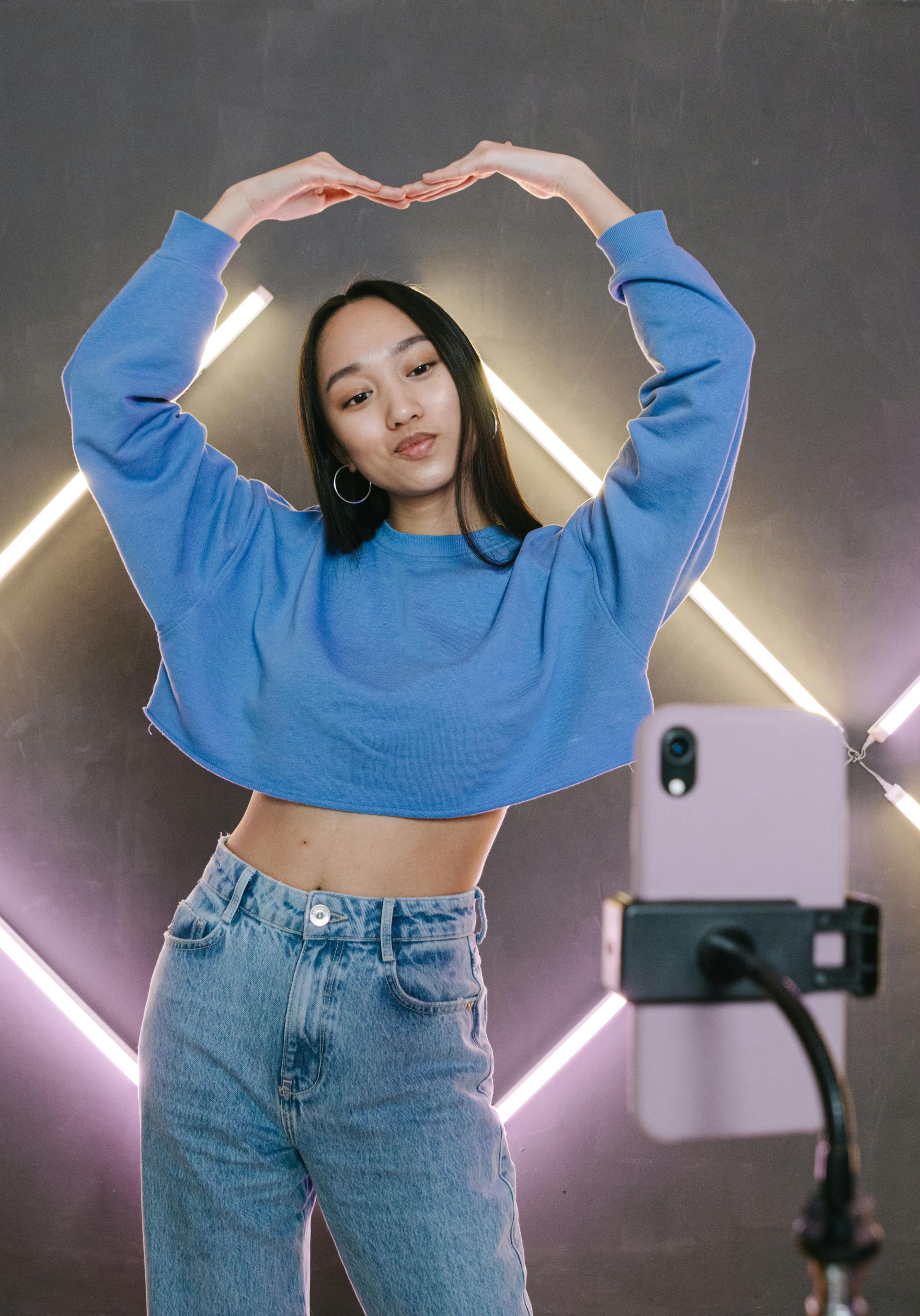 A woman in a blue sweater is making a heart shape with her hands.