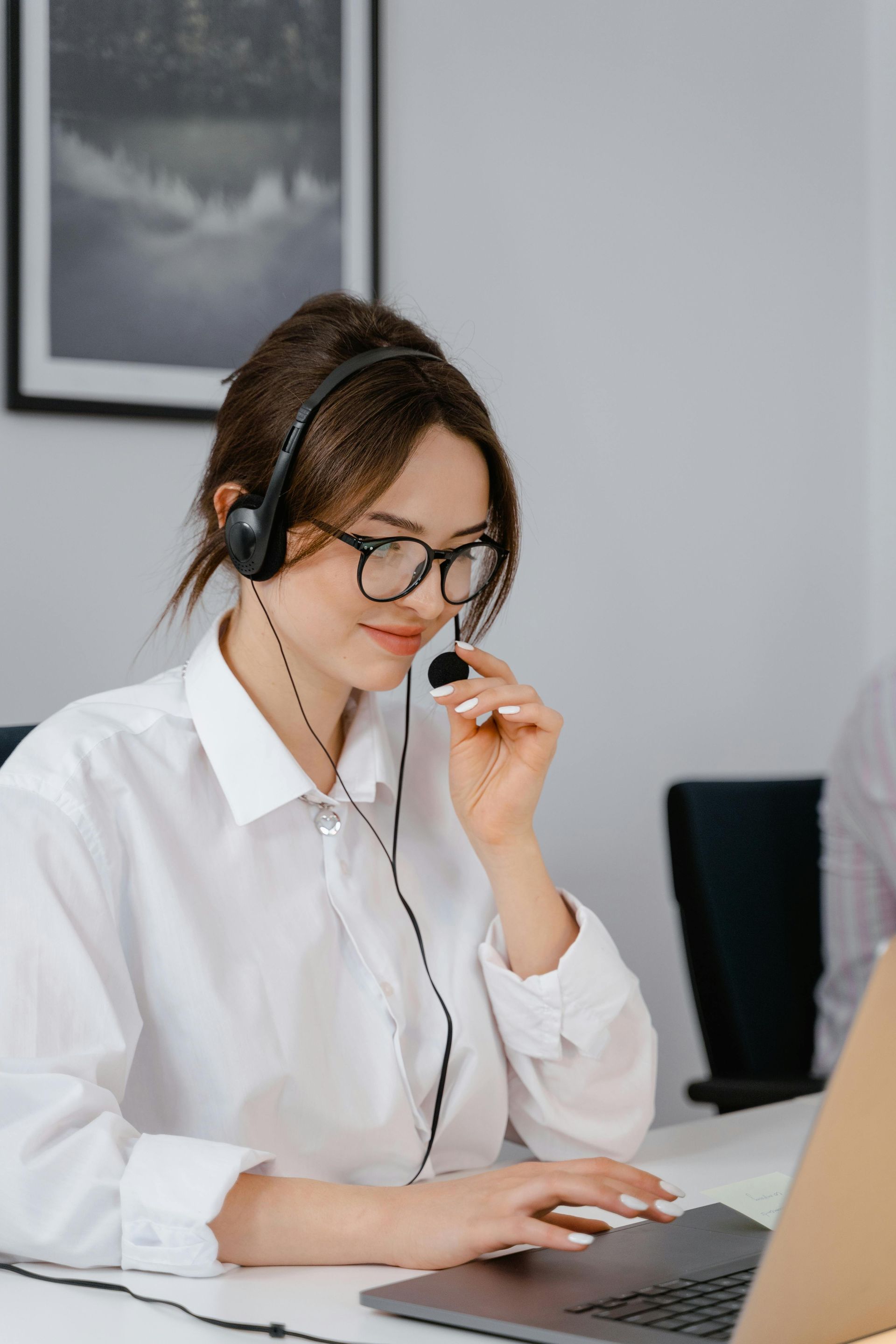 Woman with headset and glasses working on a laptop in an office setting.