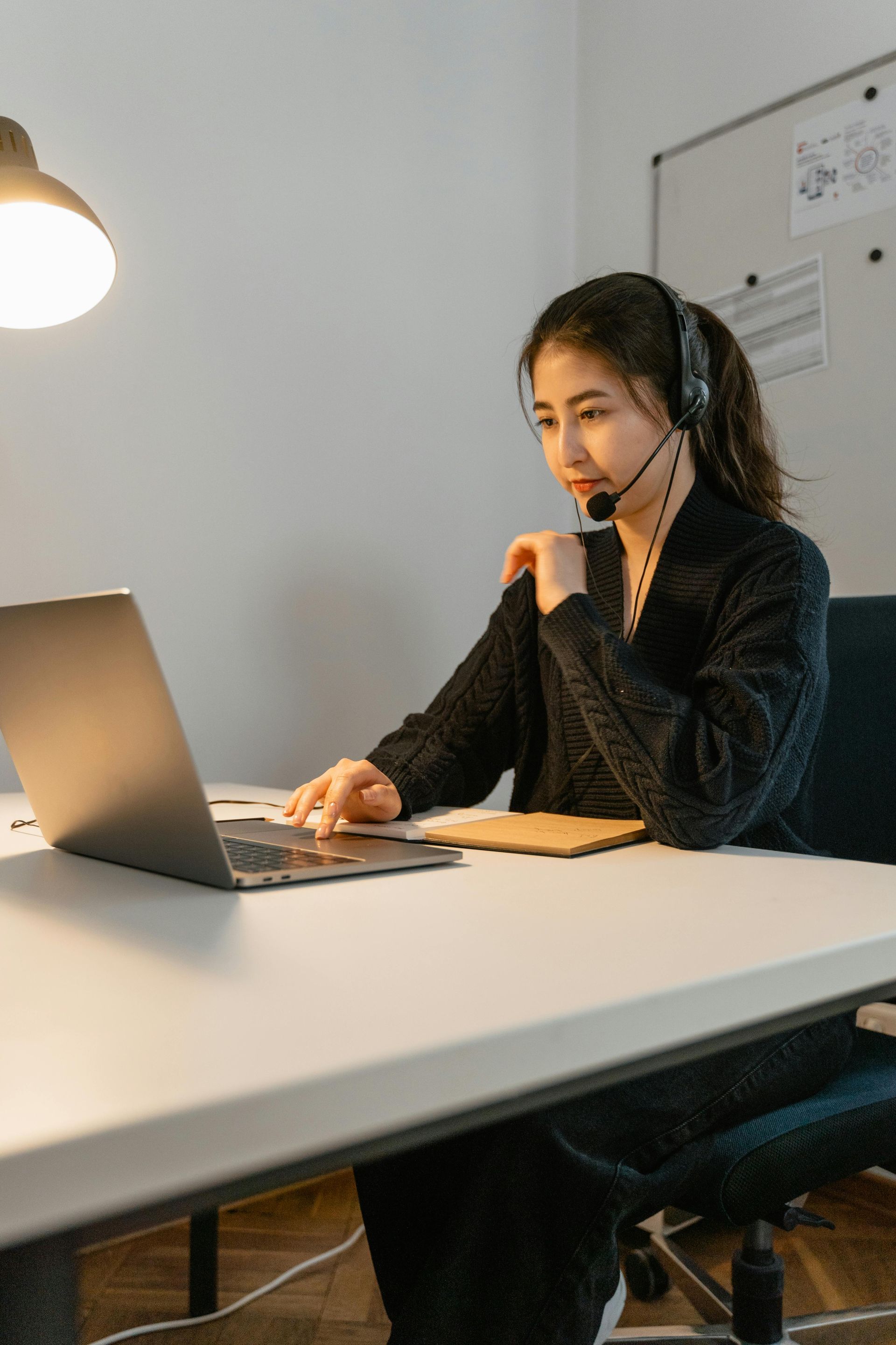 A woman wearing headphones is sitting at a desk using a laptop computer.