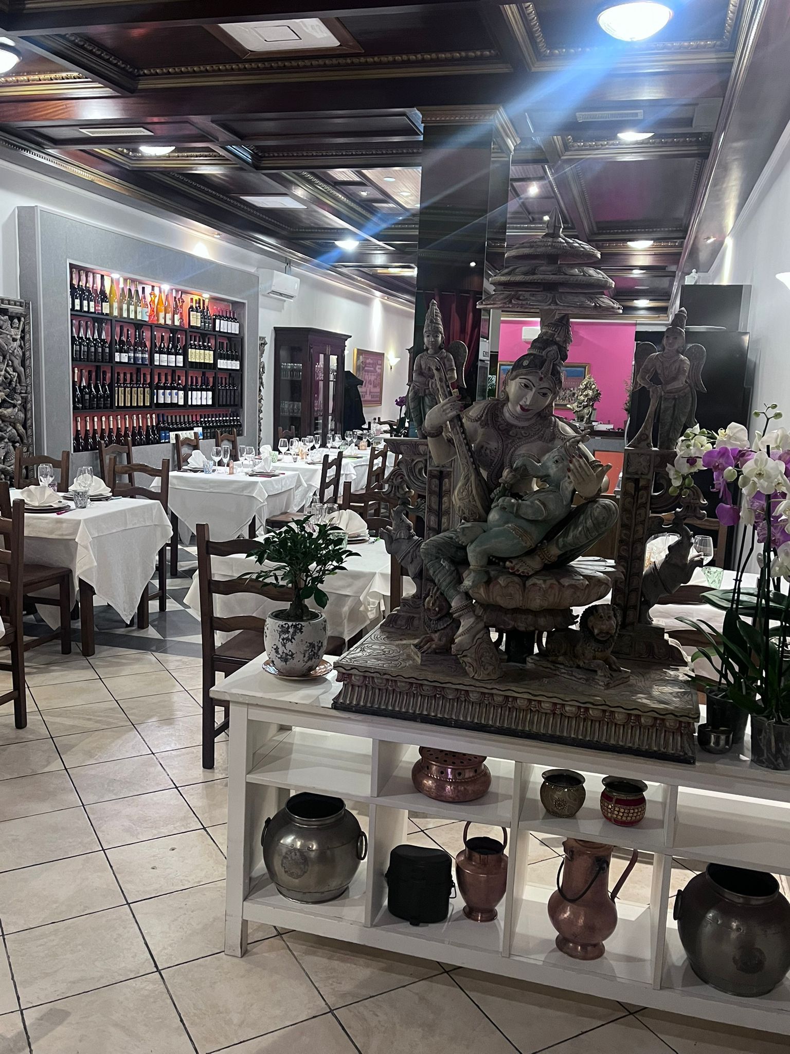 Interno di un negozio decorato con sculture in pietra, scaffali con oggetti d'arredo e tavoli da pranzo sotto luminose luci a soffitto.