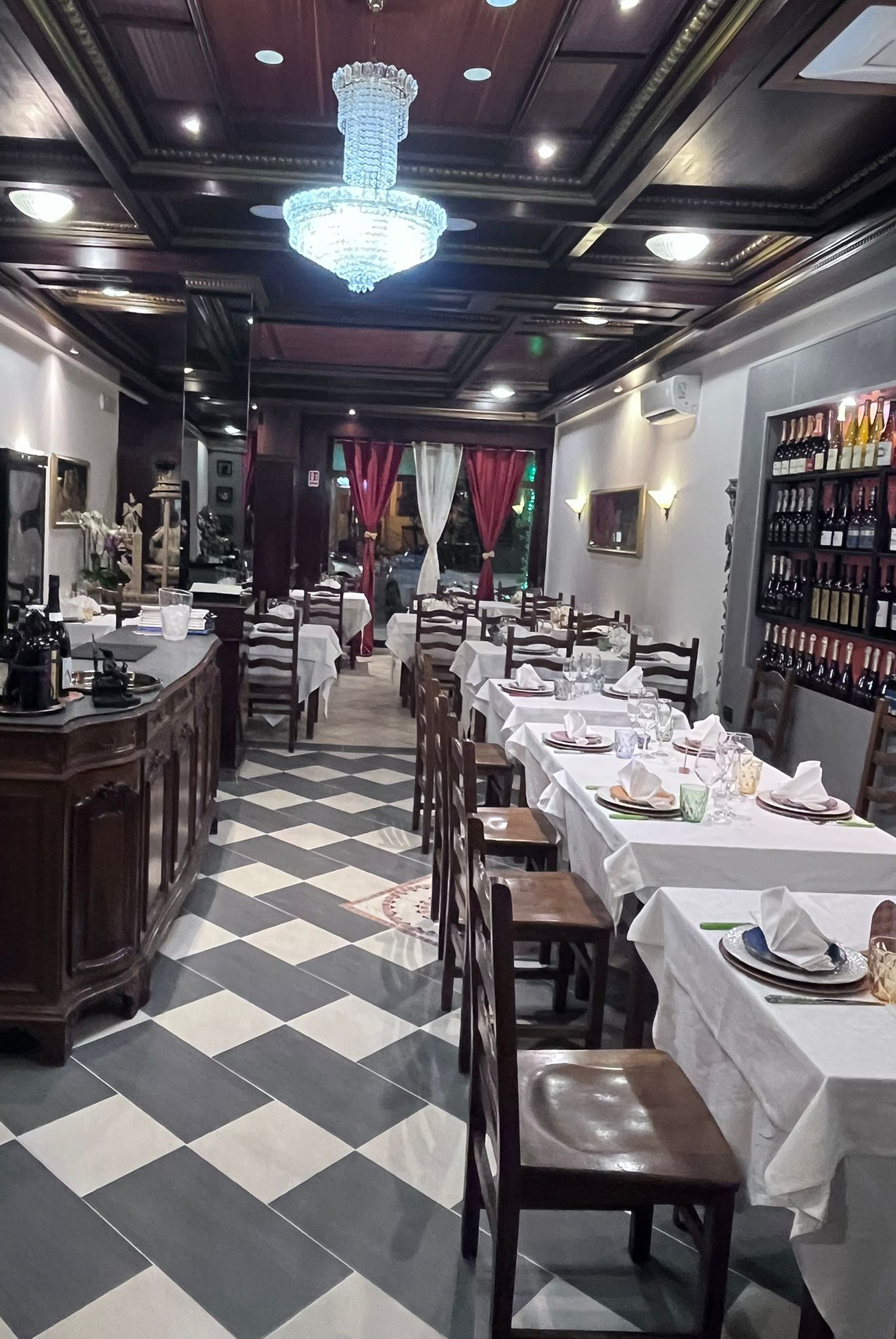Elegante interno del ristorante con pavimento a scacchi, lampadari e tavoli apparecchiati con cura.