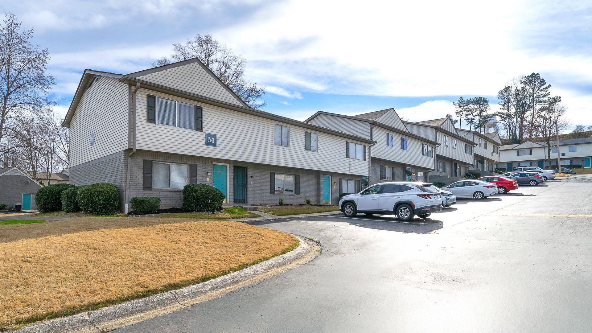 Row of apartments  with white siding, teal doors, and a parking lot.
