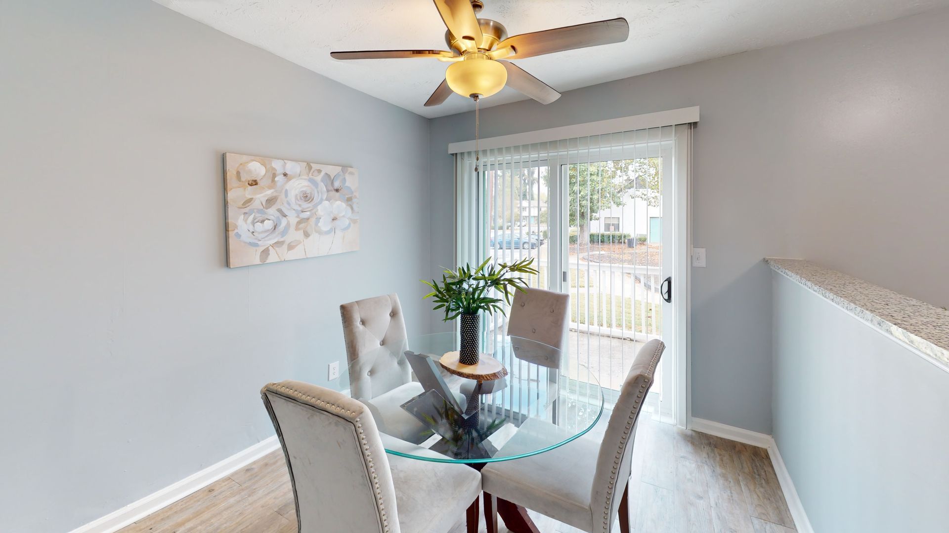 Empty room with wood-look flooring, white walls, a window with blinds, and an open doorway to a balcony.