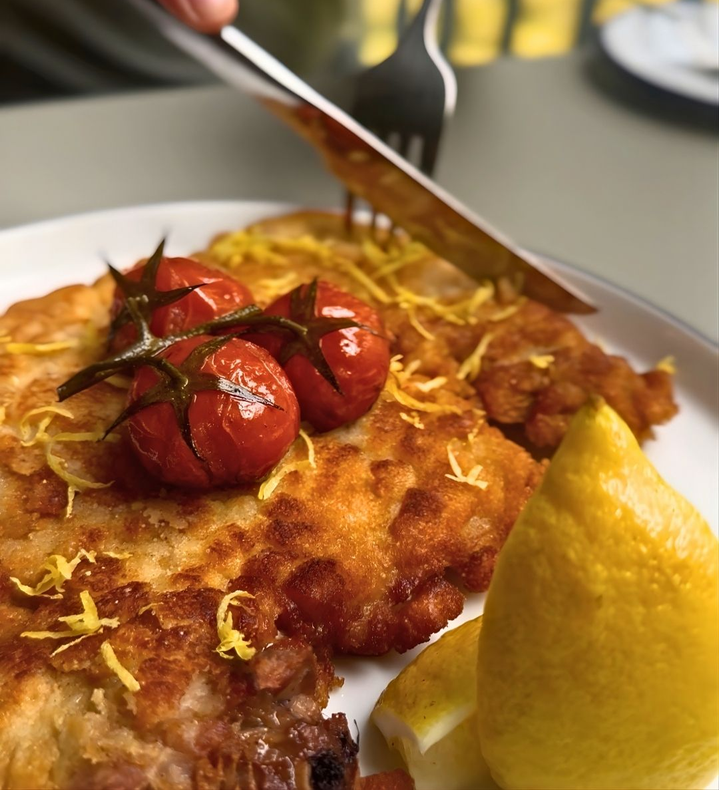 Entrada empanada dourada, coberta com tomates assados ​​e fatias de limão, servida em um prato branco.