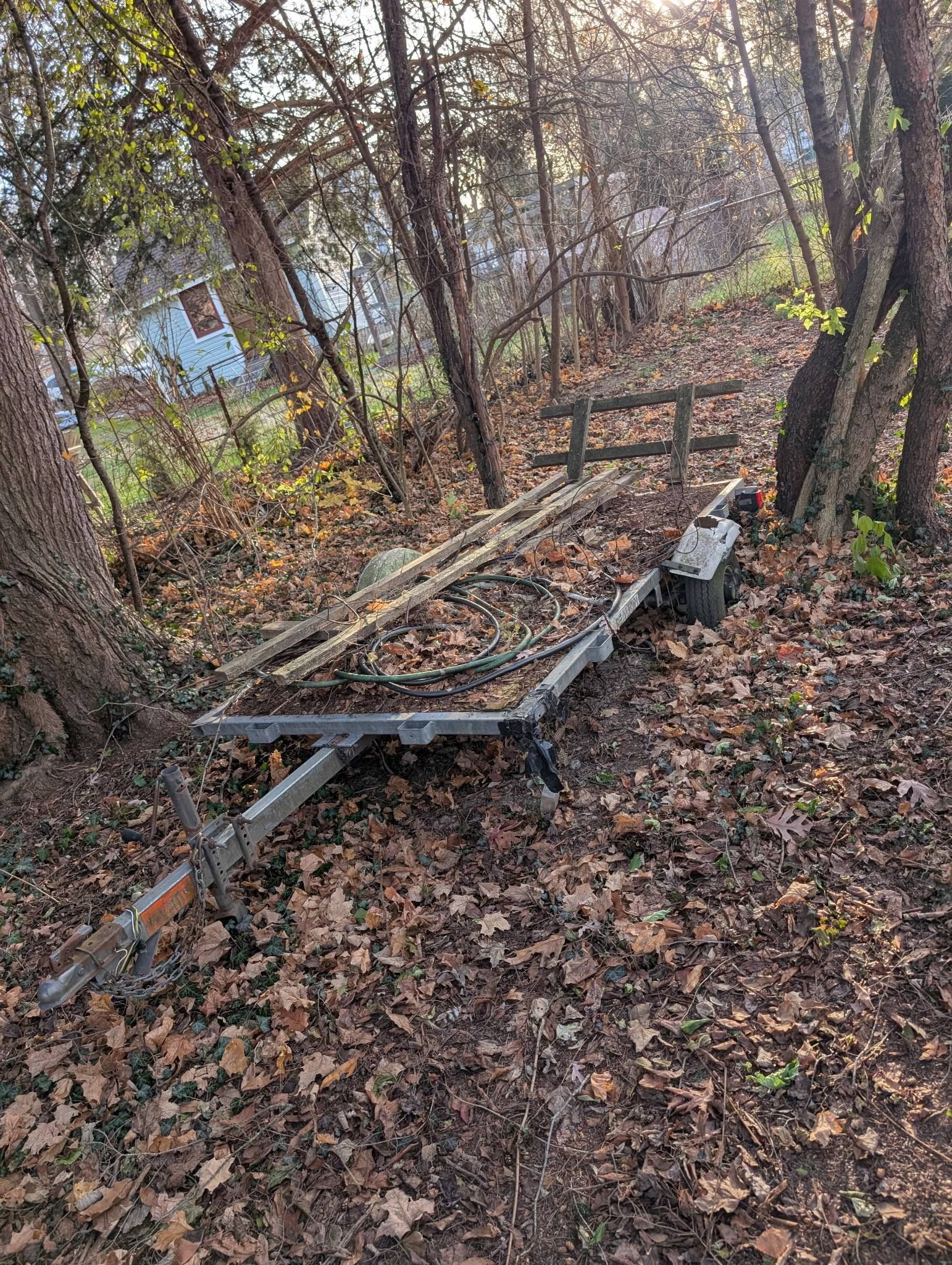 Boat trailer on a leaf-covered path in a wooded area.