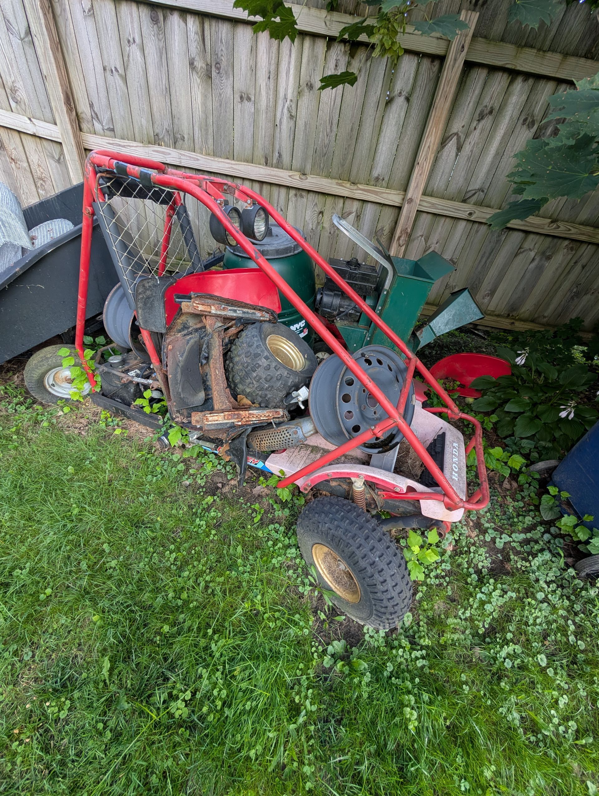 Red frame off-road vehicle with wheels and debris in overgrown grass.