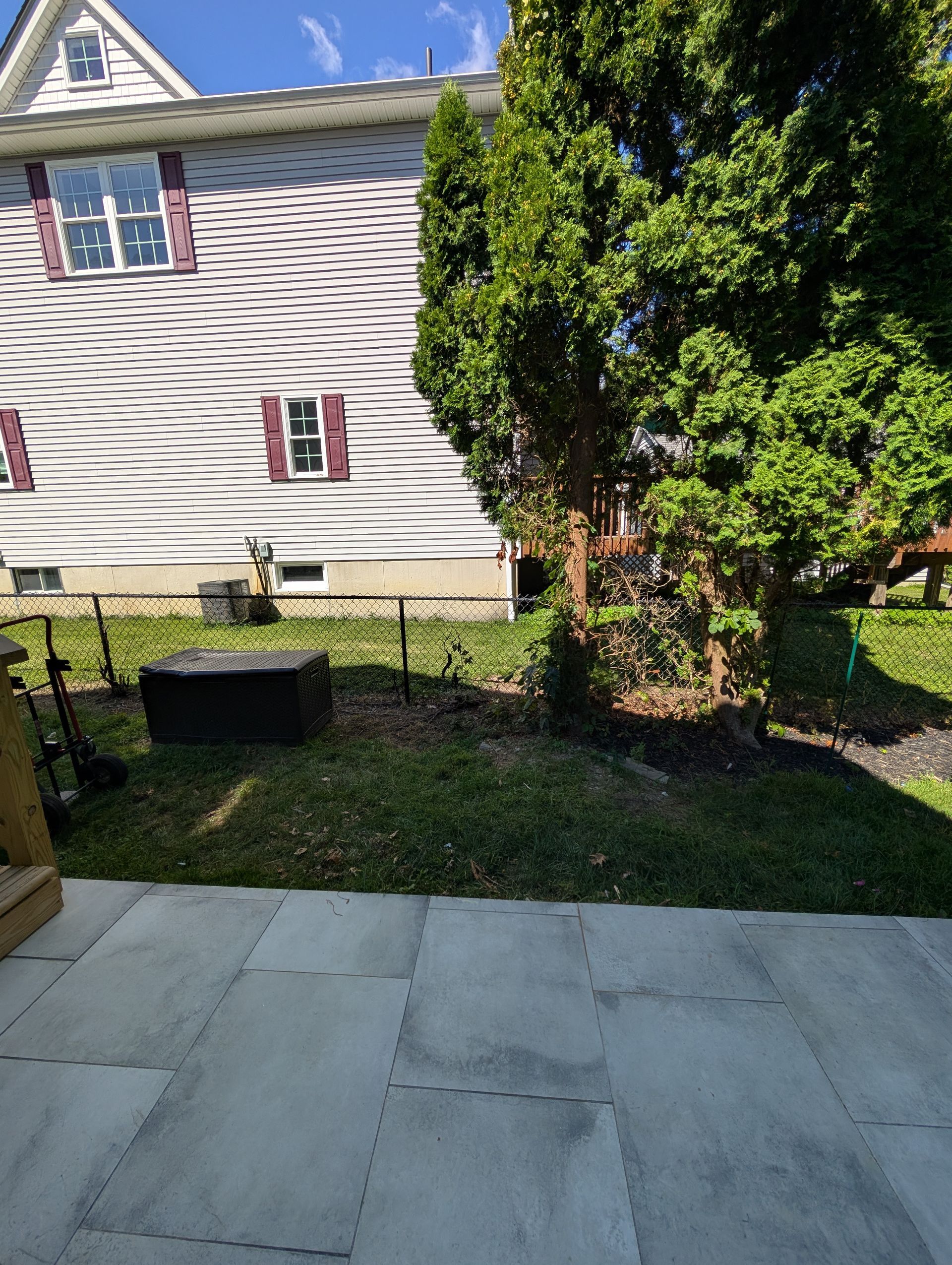 Backyard patio with gray stone tiles, grass, and a house with wavy siding.