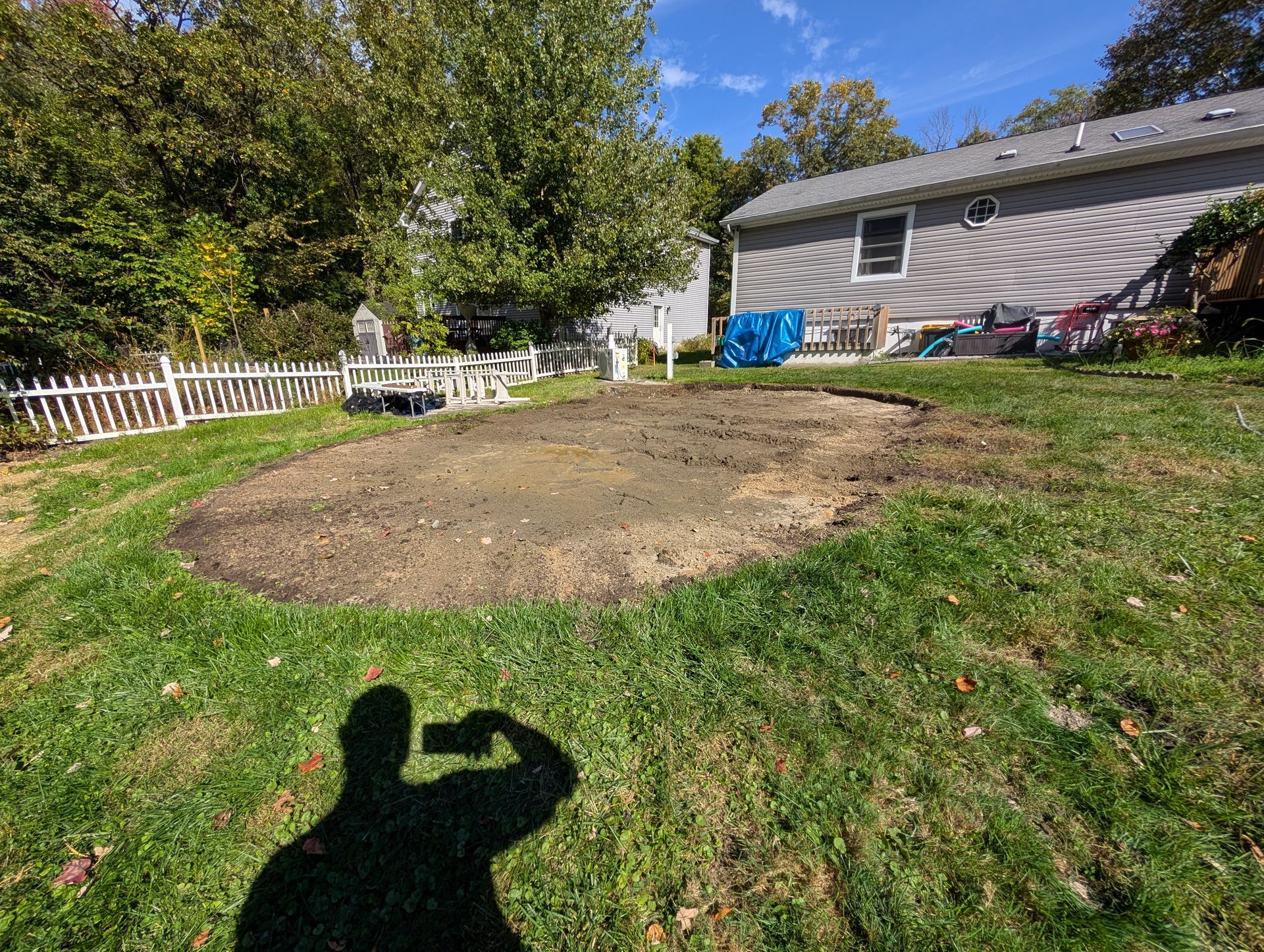 Backyard with a dirt patch where a pool was, surrounded by grass and a white fence. A house is in the background.