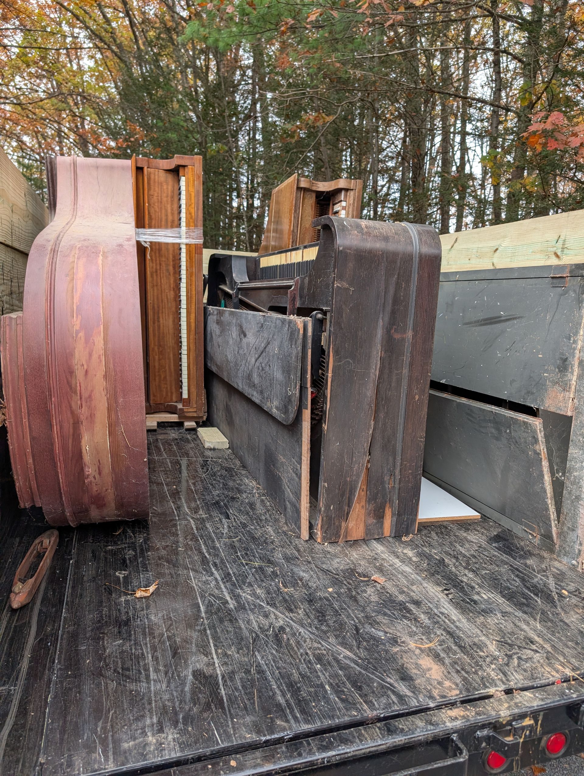 Deconstructed piano parts loaded in a flatbed trailer, with wood and debris visible.