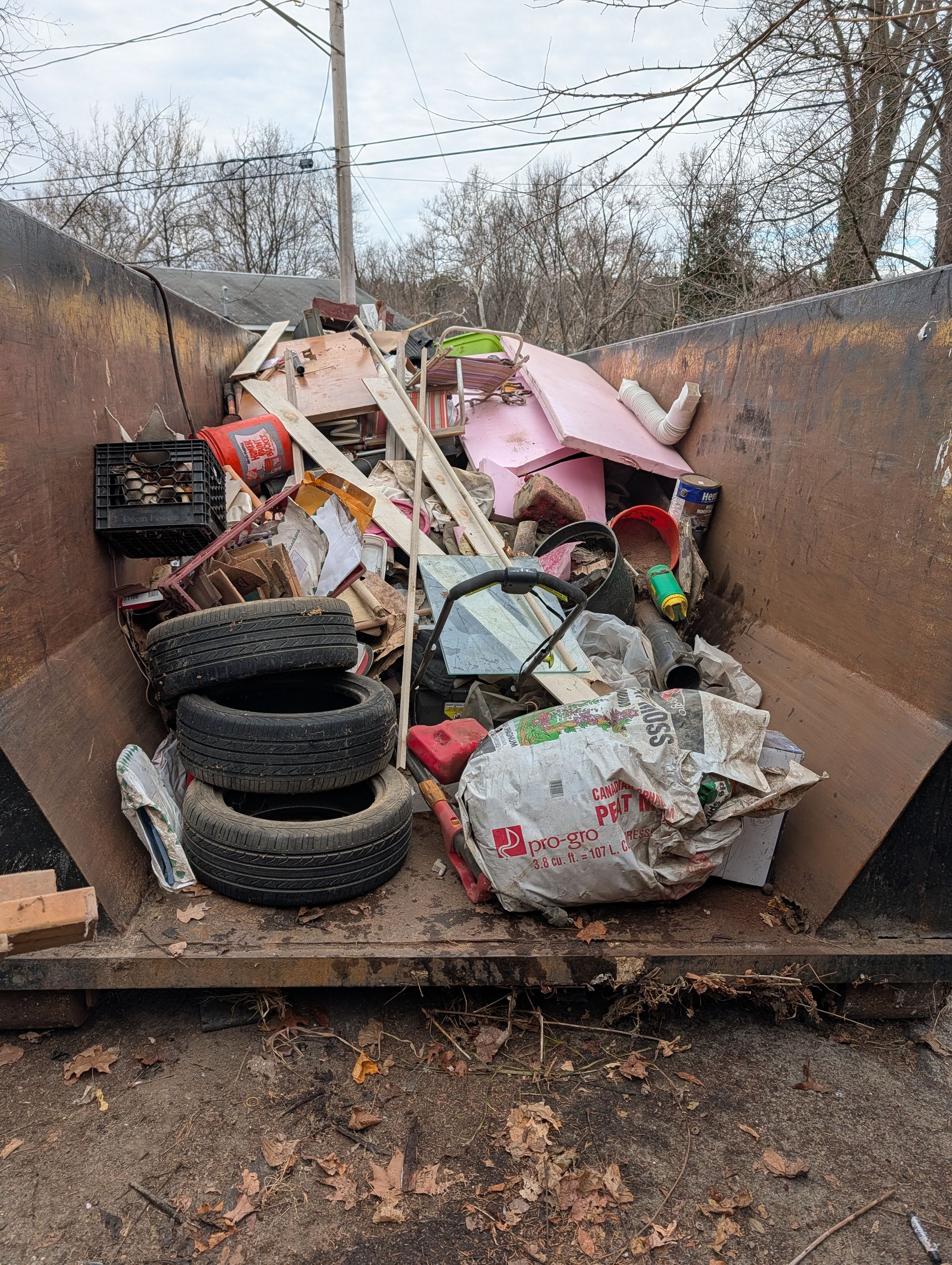 Dumpster filled with trash and debris, including tires, wood, and a pink object.