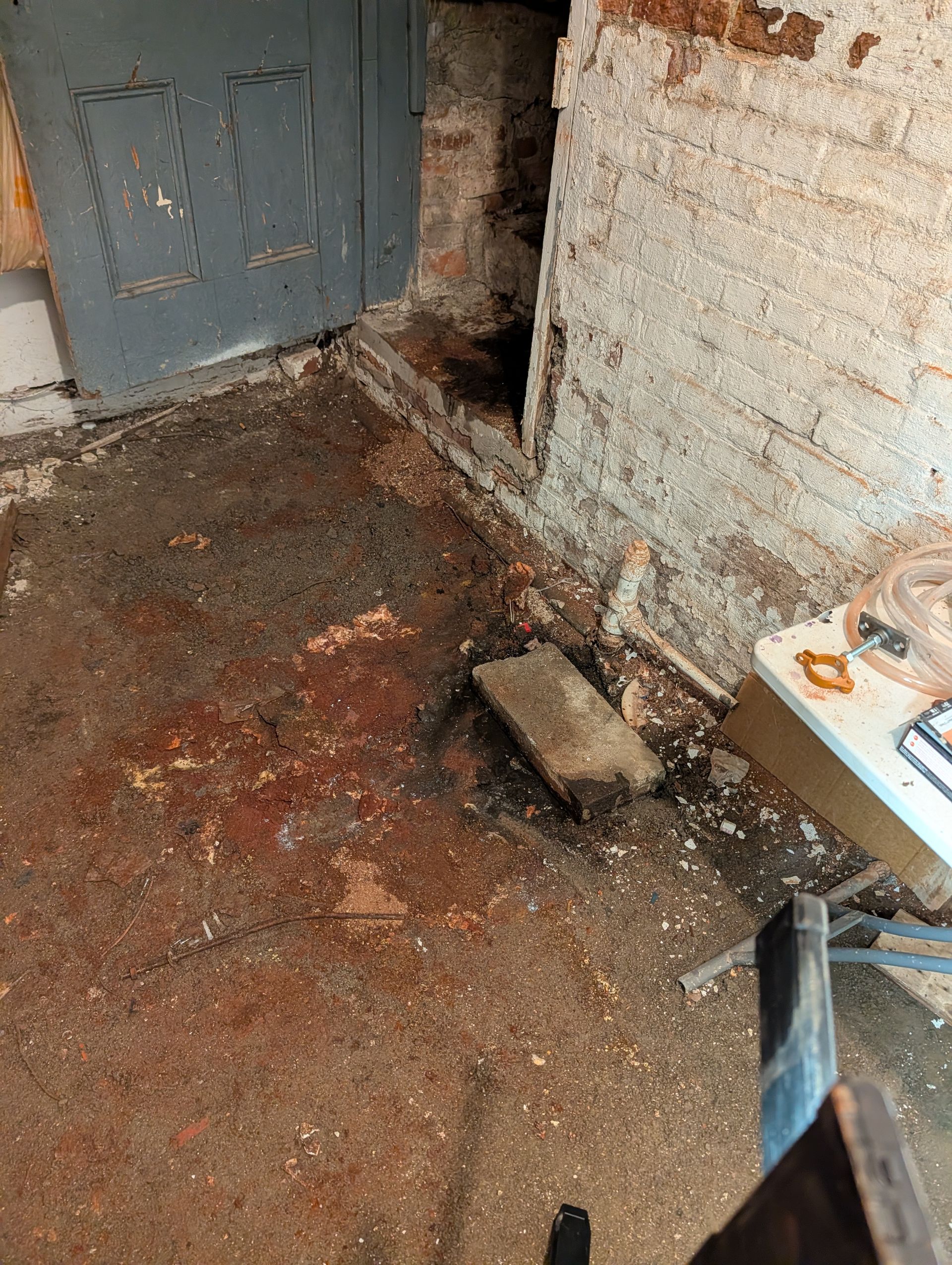 Basement floor with water damage near a door and crumbling walls.