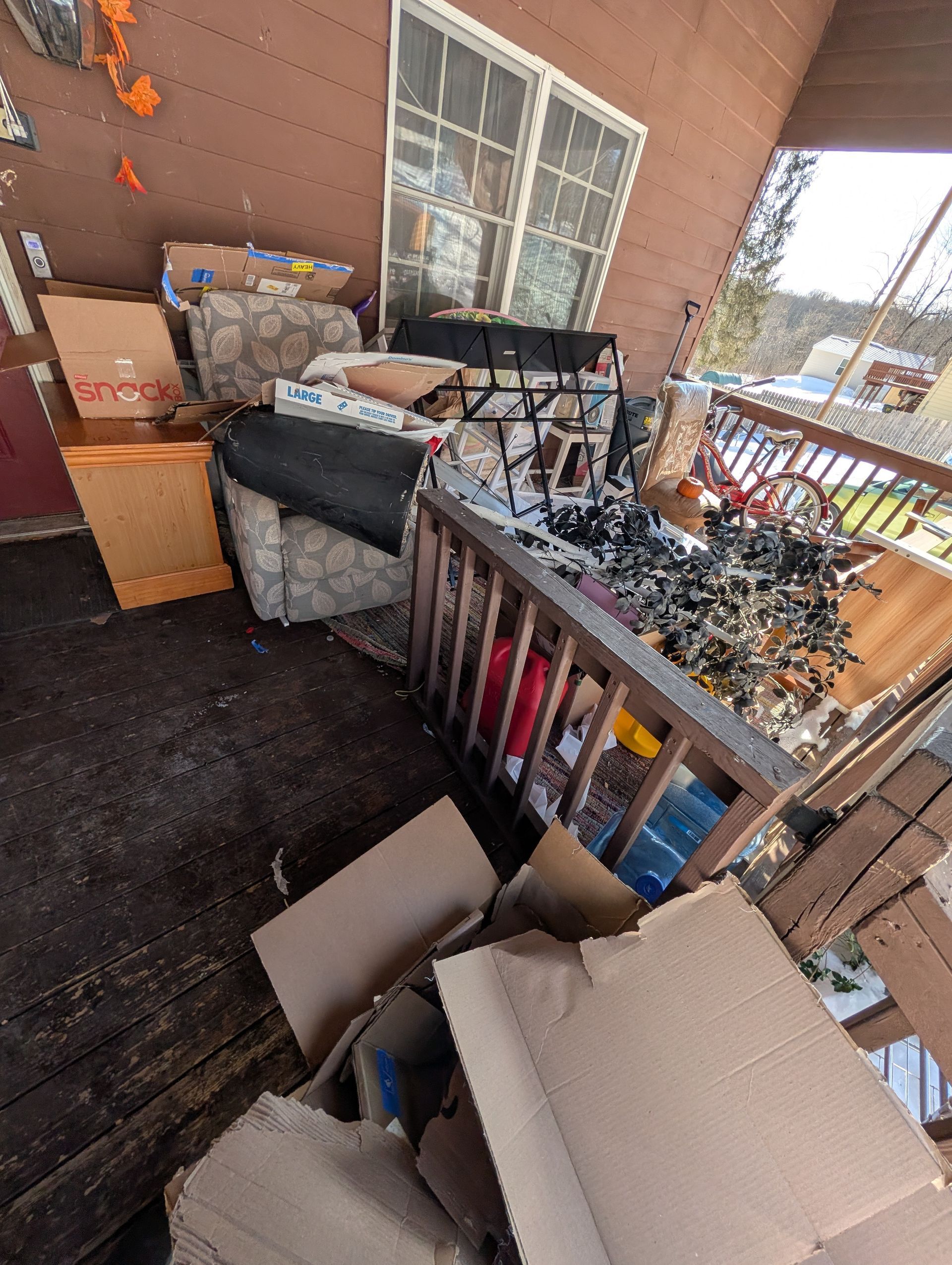 Porch cluttered with boxes, furniture, and debris. Brown siding and railing visible.