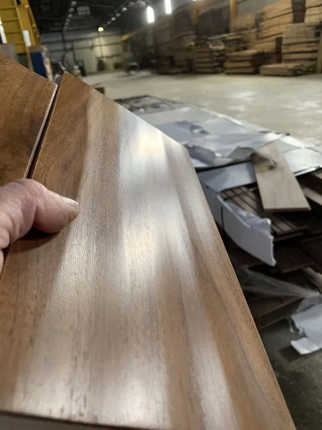Hand holding a wood veneer sheet in a warehouse with stacked materials in the background