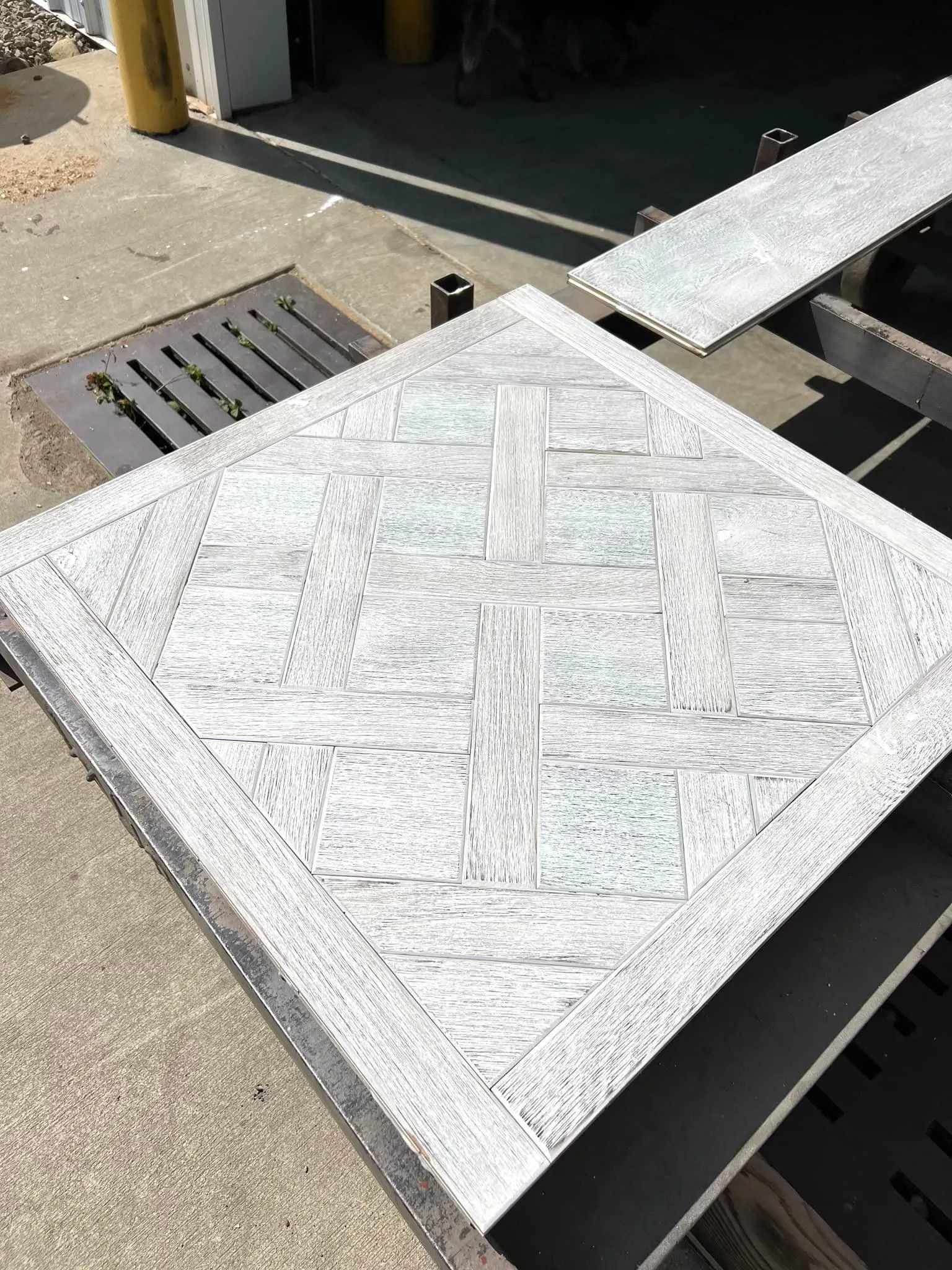 A white square panel with a cross-braced pattern lies on a concrete surface near a drain and ramp.