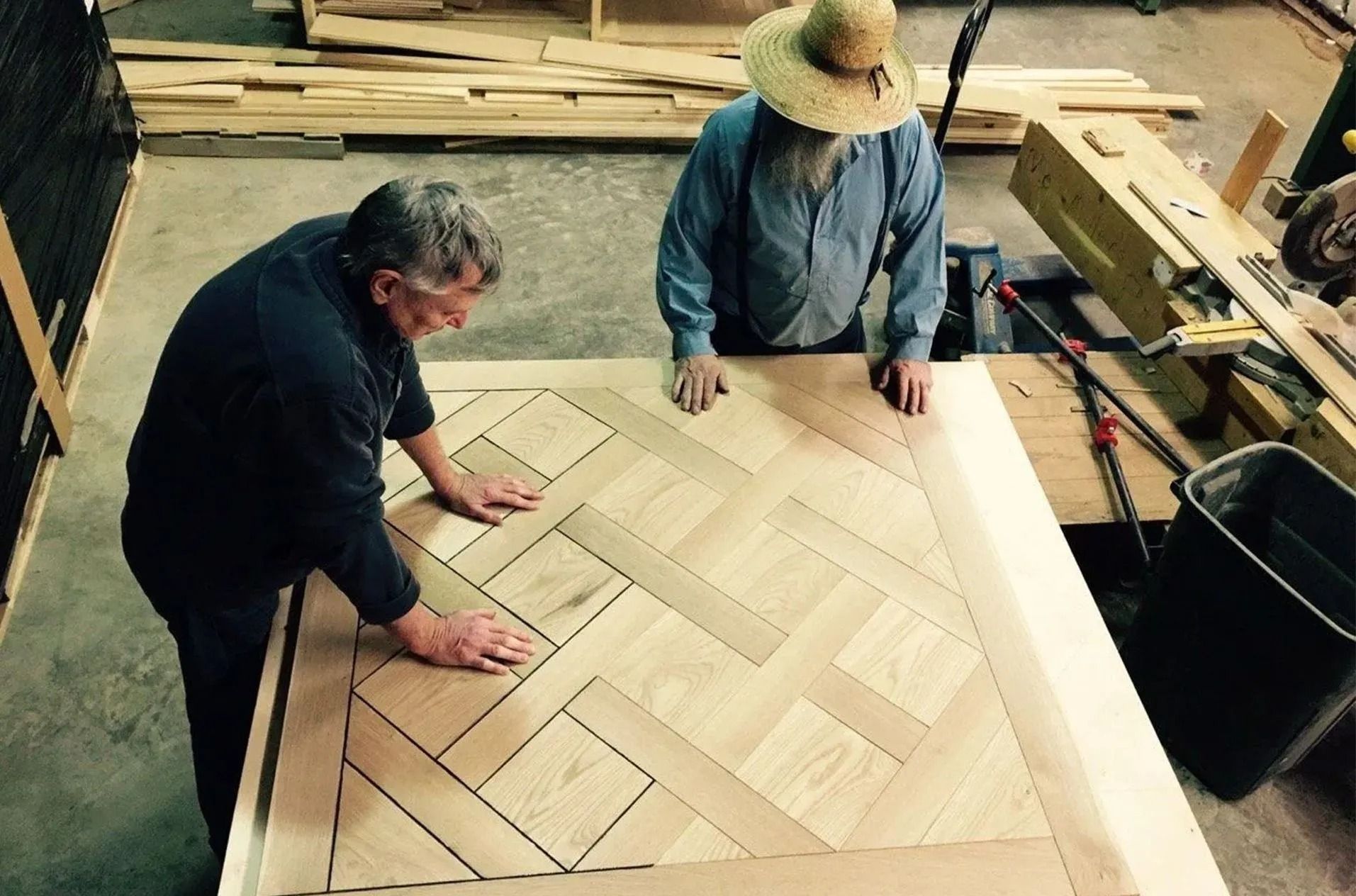 Two workers assembling a herringbone wooden floor in a workshop