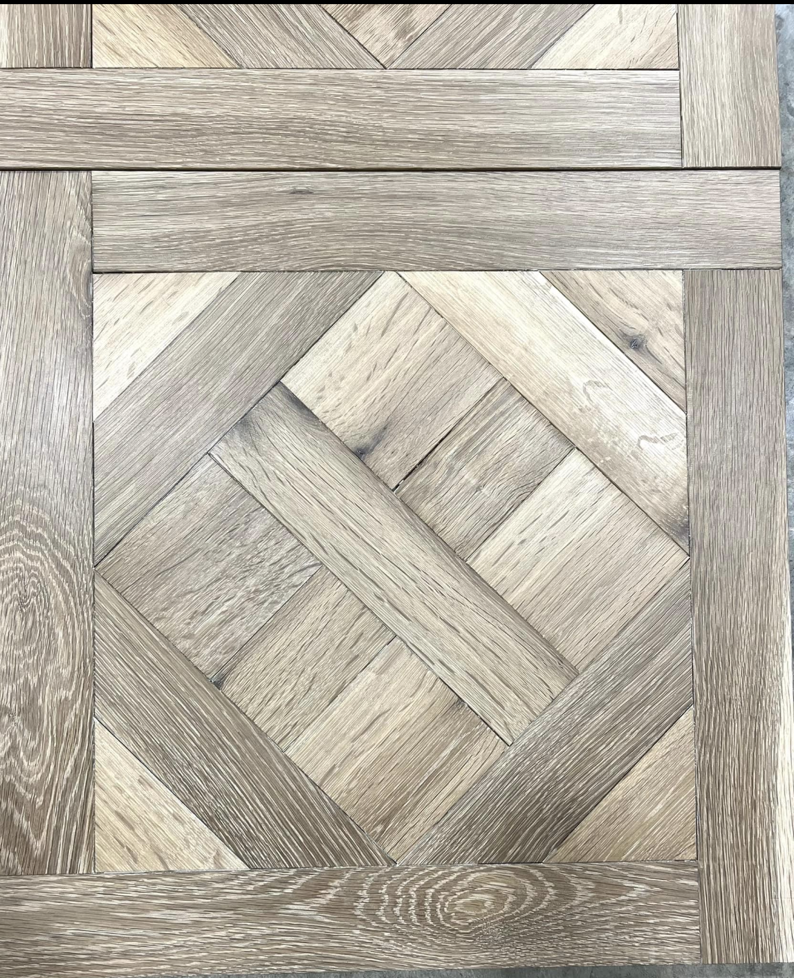 Close-up of a woven wood or laminate parquet pattern in gray and beige tones.