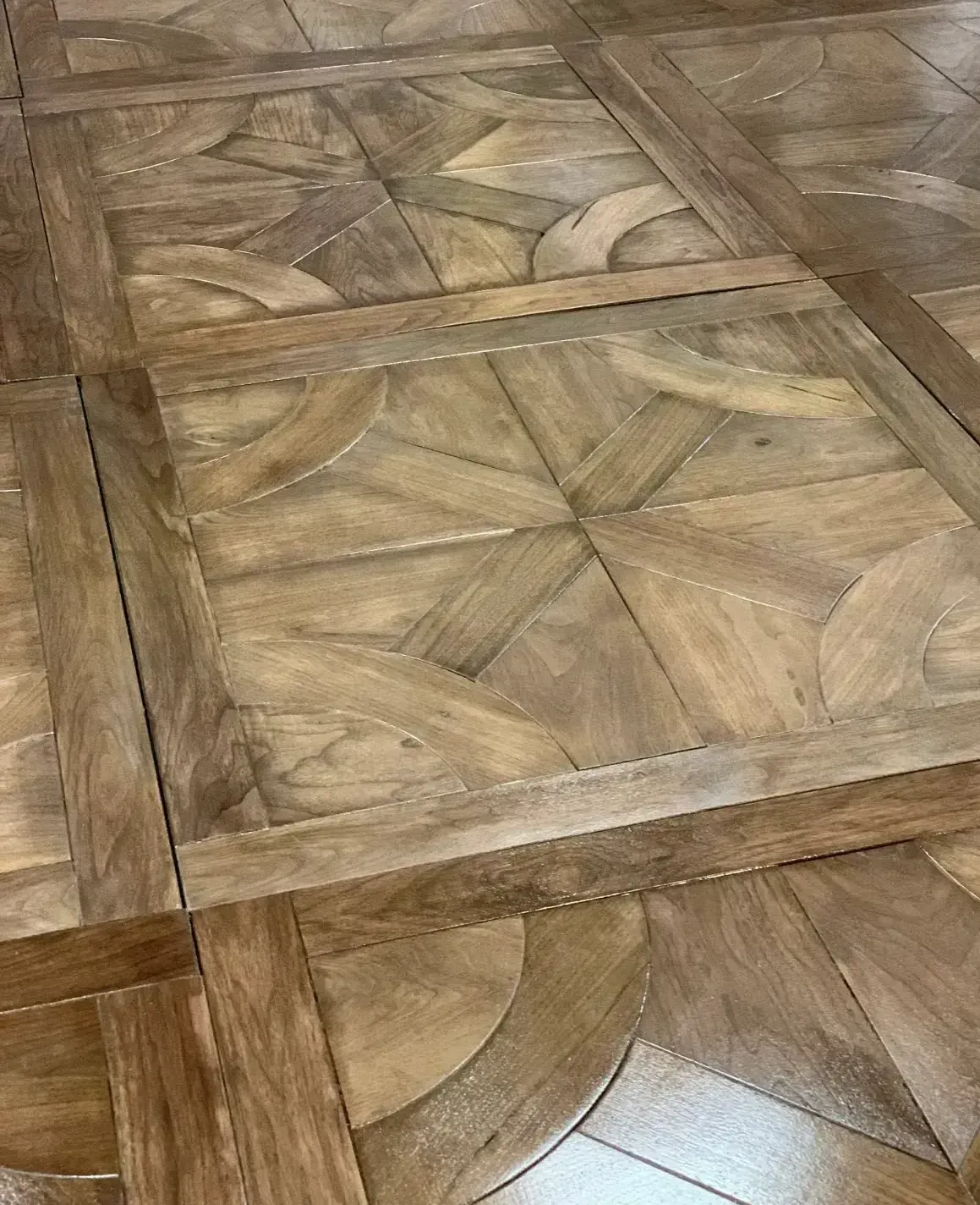 Close-up of a wooden parquet floor with geometric tile patterns and a glossy finish
