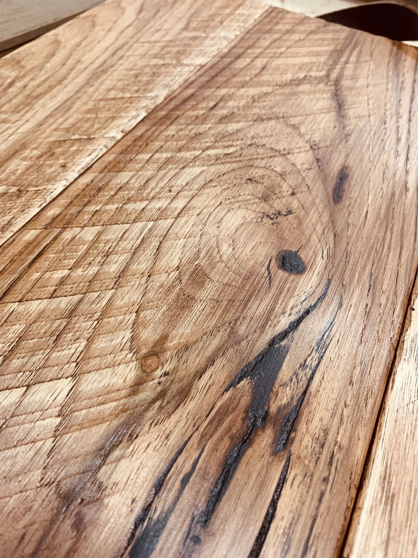 Close-up of a rustic wooden surface with visible grain, knots, and dark streaks.