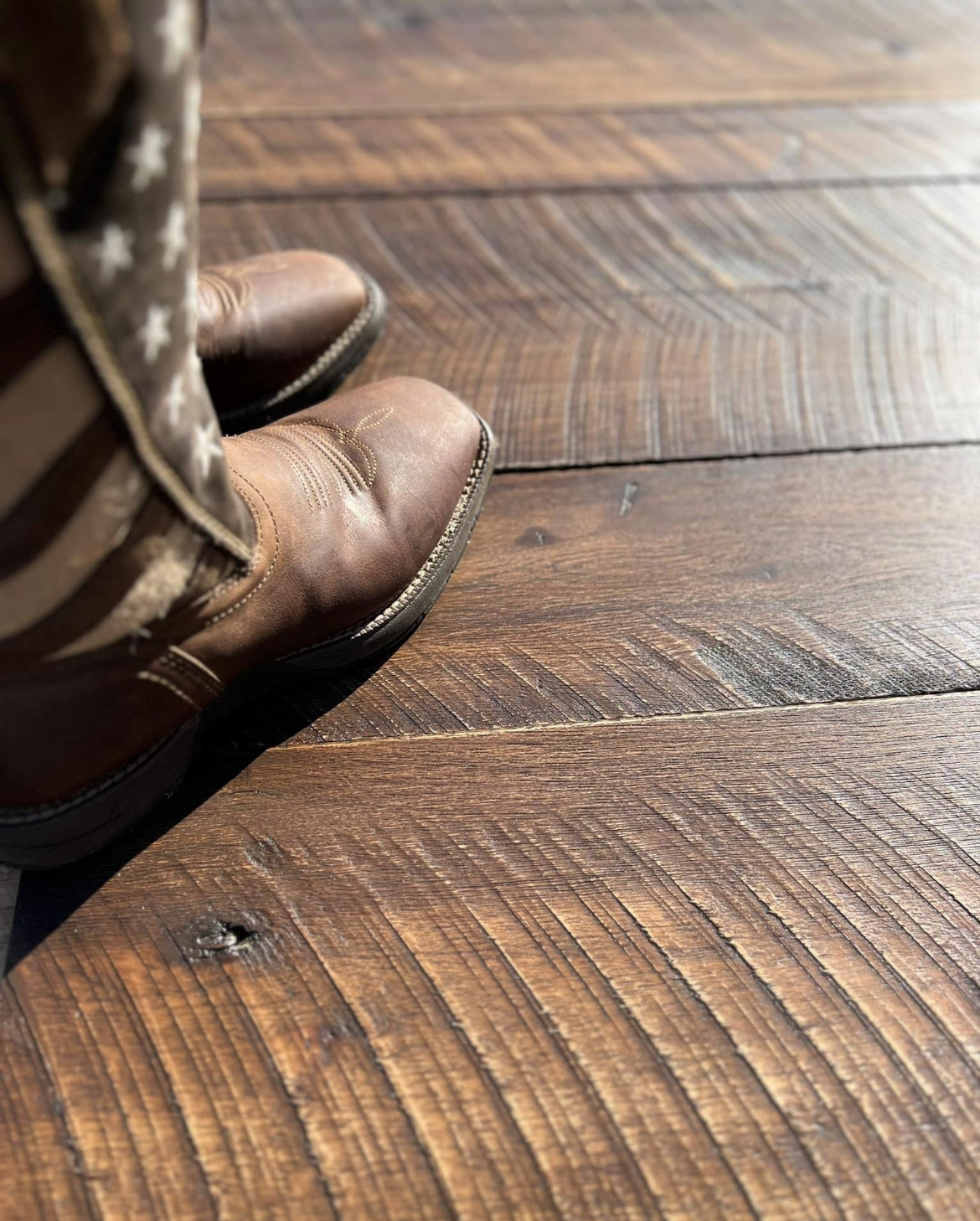 Brown leather boots on a sunlit wooden floor, with camouflage pants visible.