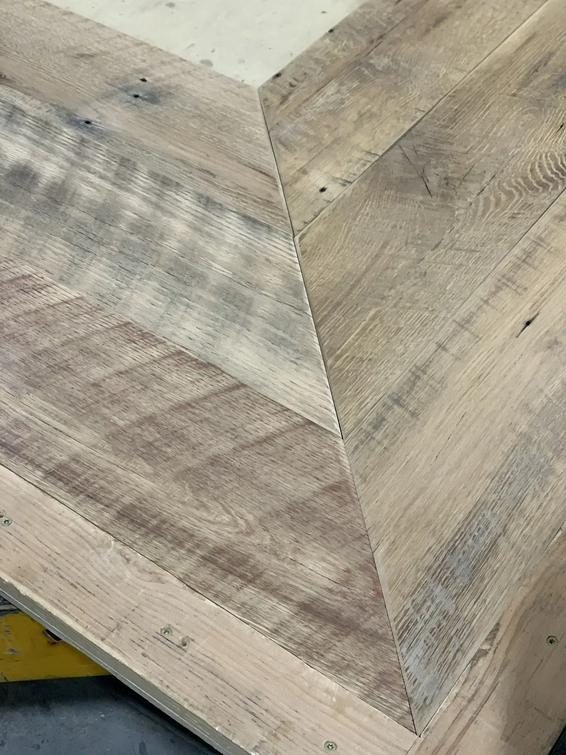Close-up of a light wood herringbone tabletop corner with gray and beige tones