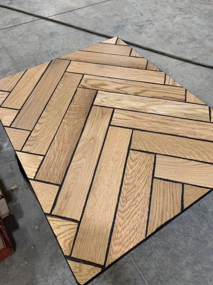 Hexagonal wood-pattern tile sample with tan chevron planks and black grout on a gray concrete floor