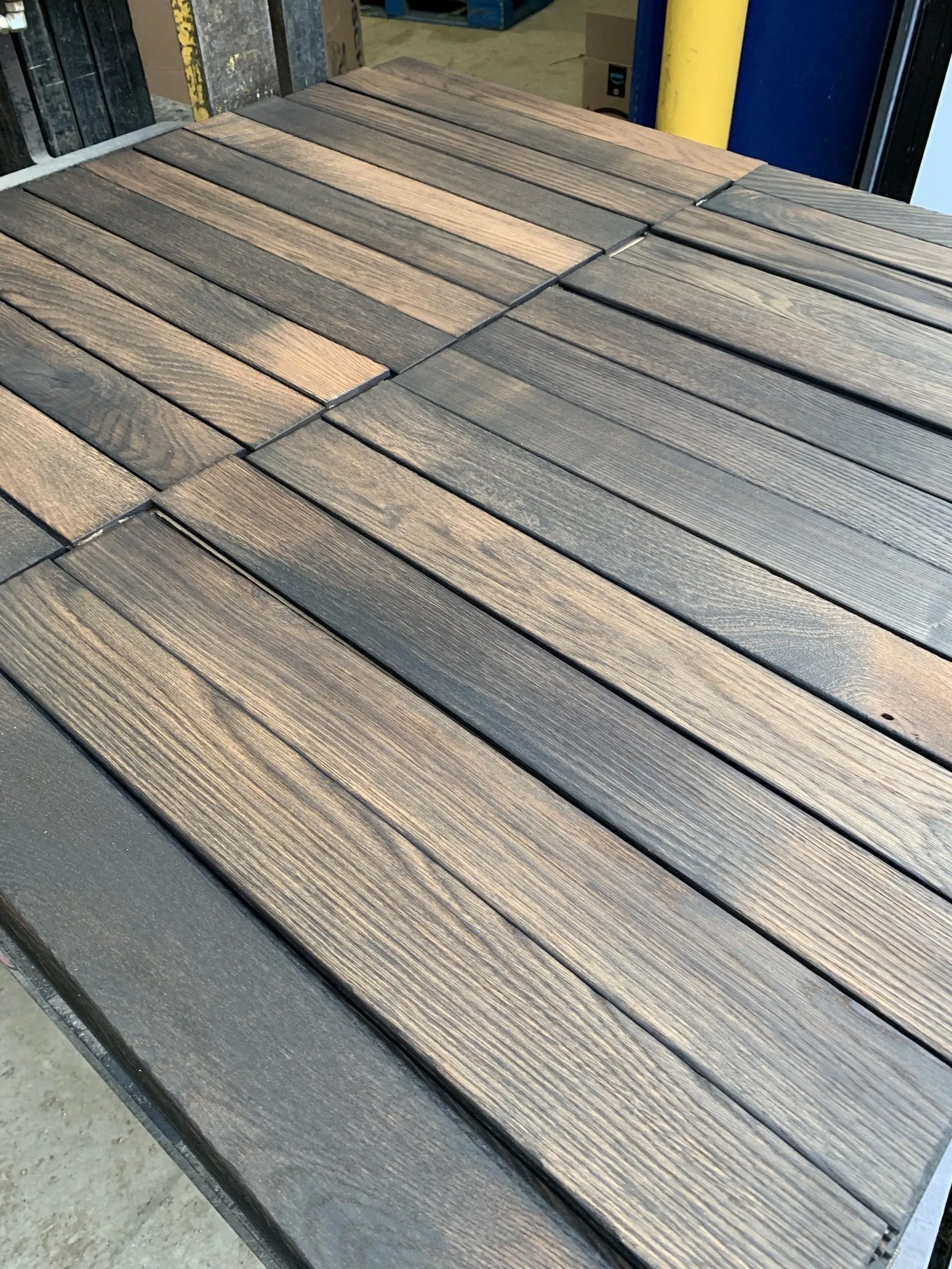 Wooden deck with gray and tan planks beside a blue wall and concrete floor.