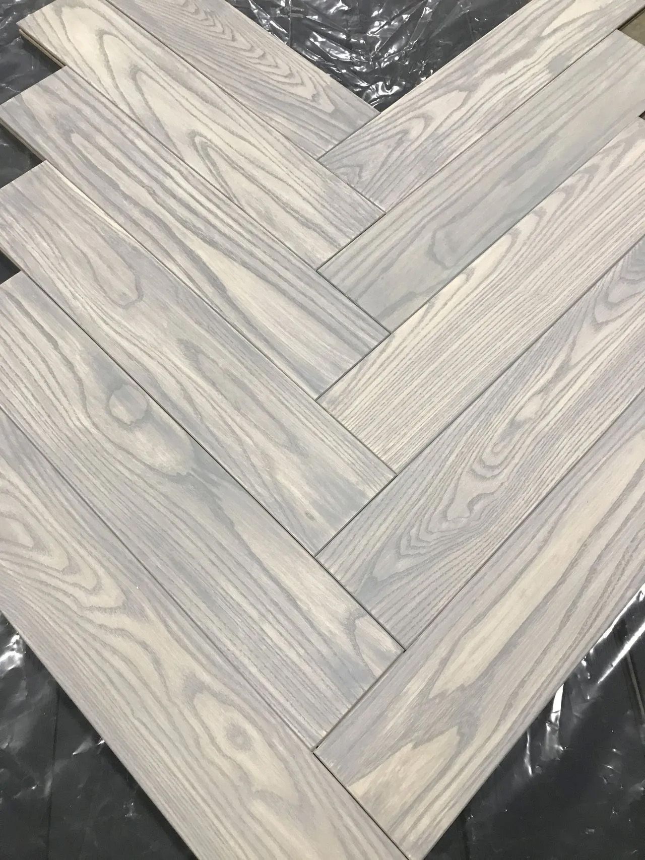 Gray wood planks arranged in a herringbone pattern on a dark surface