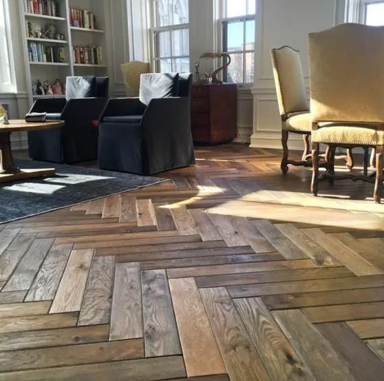Cozy living room with herringbone wood floor, black chairs, beige armchairs, and sunlight by tall windows
